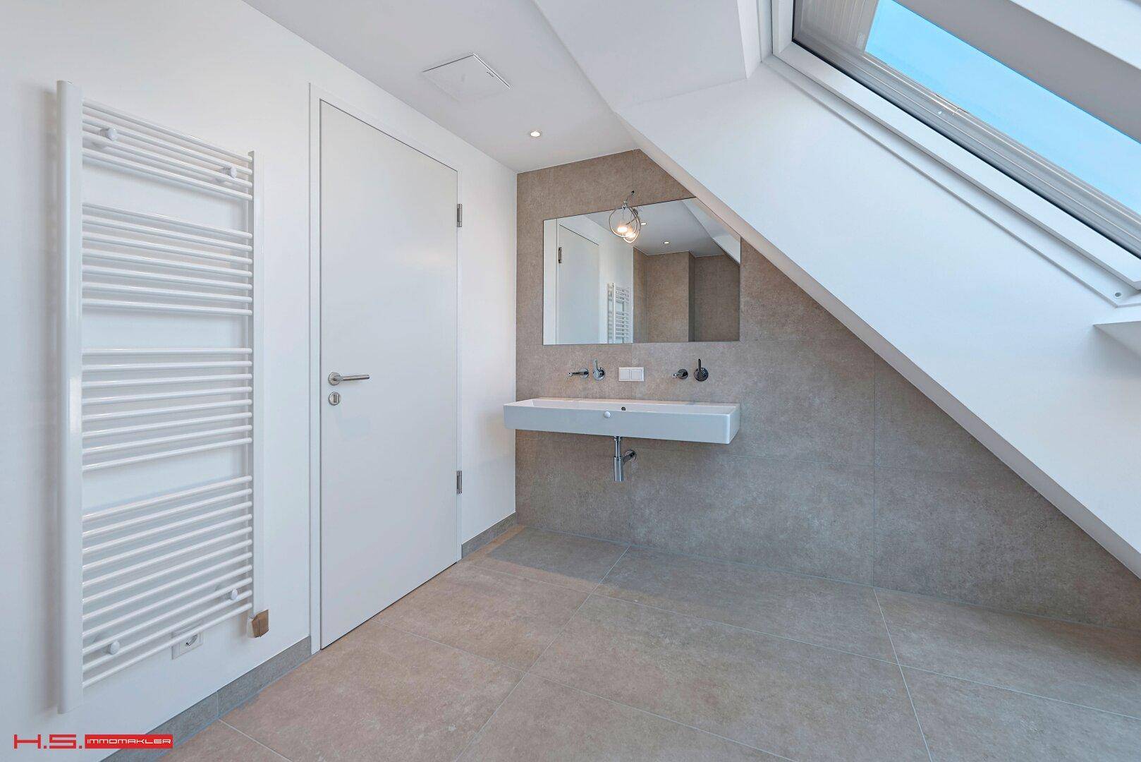 Helles Badezimmer im Dachgeschoss mit Dachfenster, beheiztem Handtuchhalter und modernem Waschtisch.