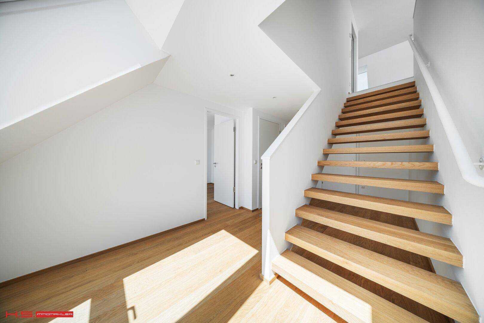 Heller Flur mit Holztreppe und Parkettboden, der die verschiedenen Ebenen der Wohnung verbindet.