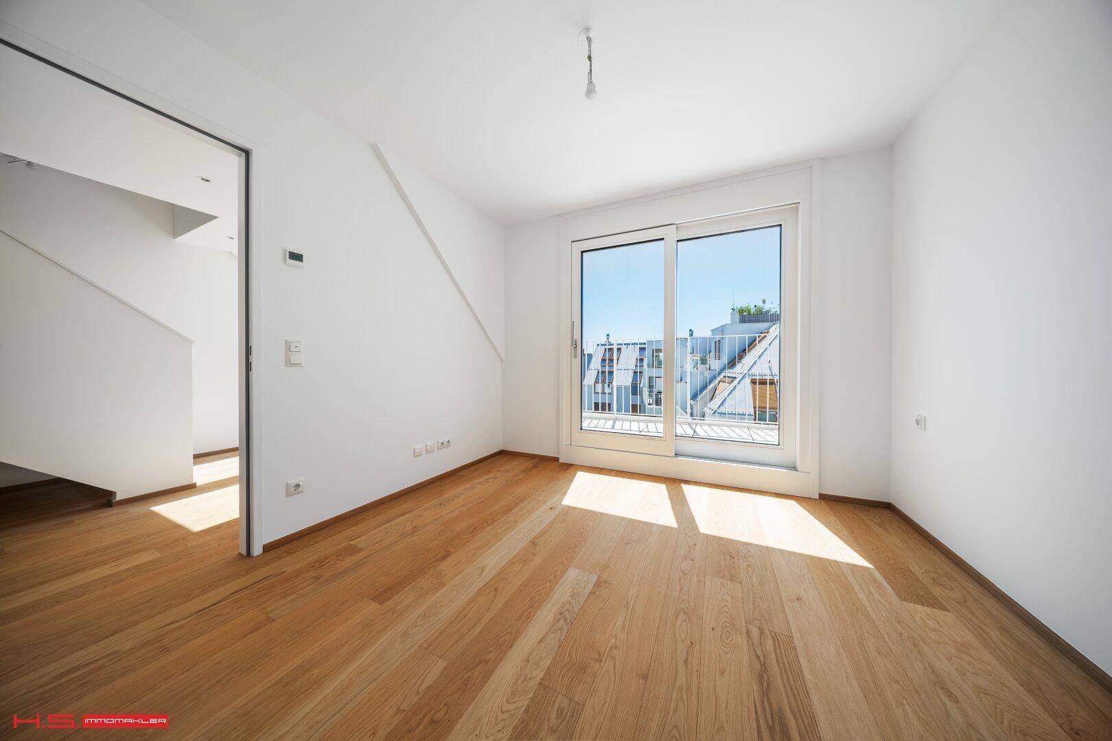 Heller Raum mit Holzboden und Schiebetür, die zu einem Außenbereich führt, ideal als Schlafzimmer.