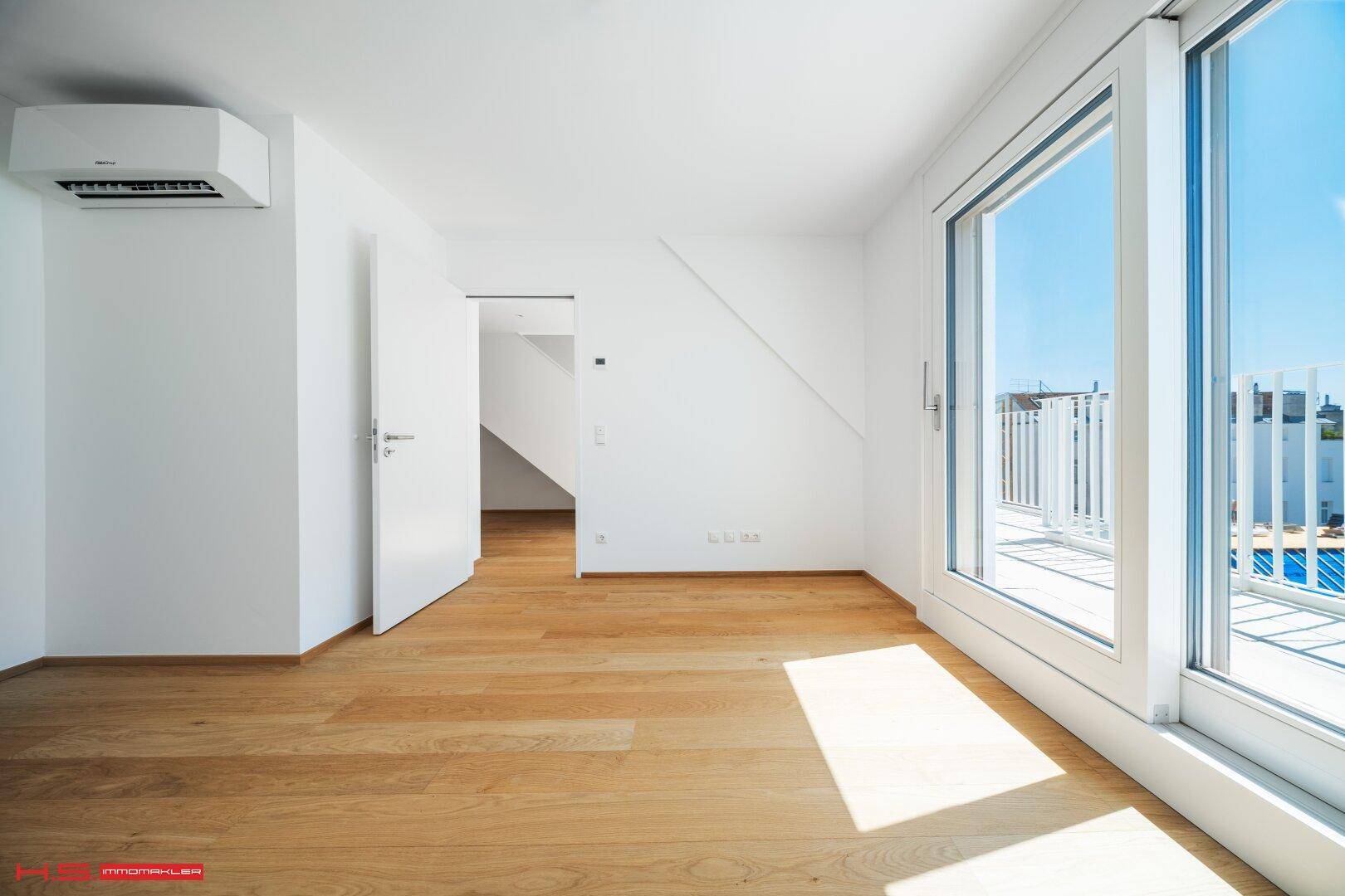 Heller Raum mit Holzboden, Klimaanlage und Zugang zu einem Balkon oder einer Terrasse.
