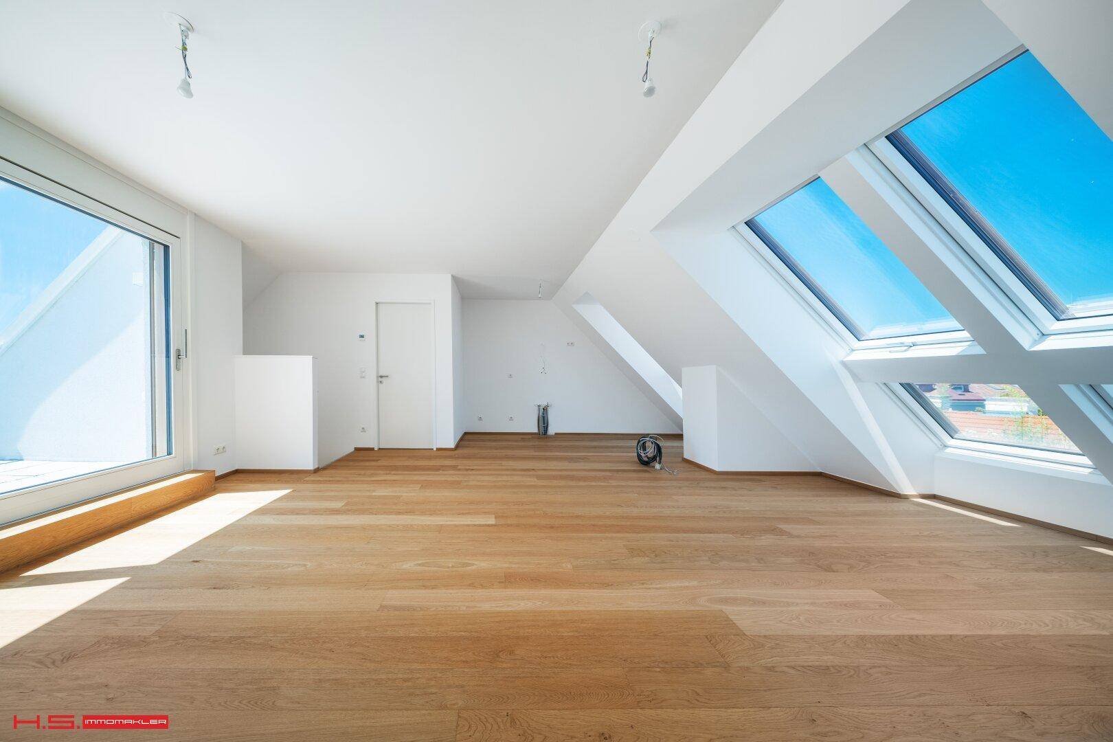 Geräumiger, heller Raum mit Holzboden und großen Dachfenstern, ideal für flexible Wohnzwecke.