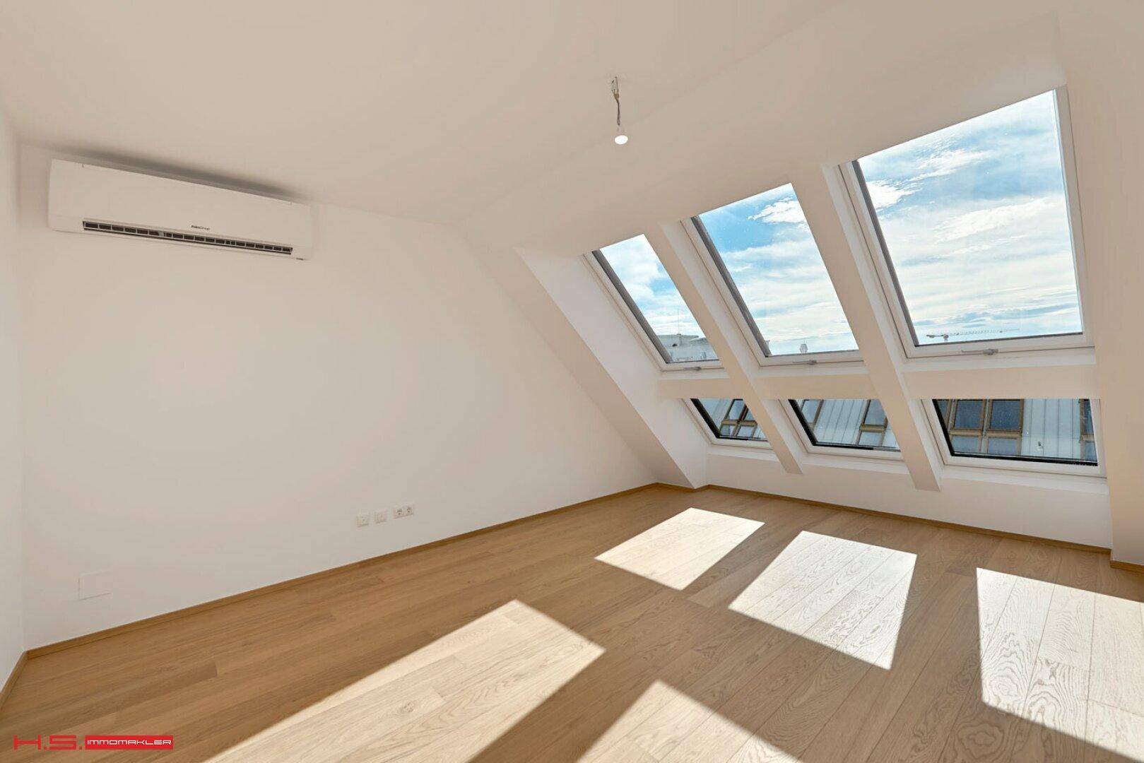 Dachgeschosszimmer mit schrägen Wänden, Holzparkett und mehreren Dachfenstern.