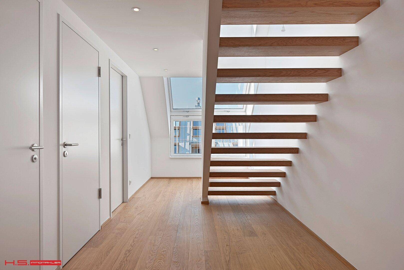 Heller Flur mit offener Holztreppe und Einbauschränken, der verschiedene Ebenen verbindet.