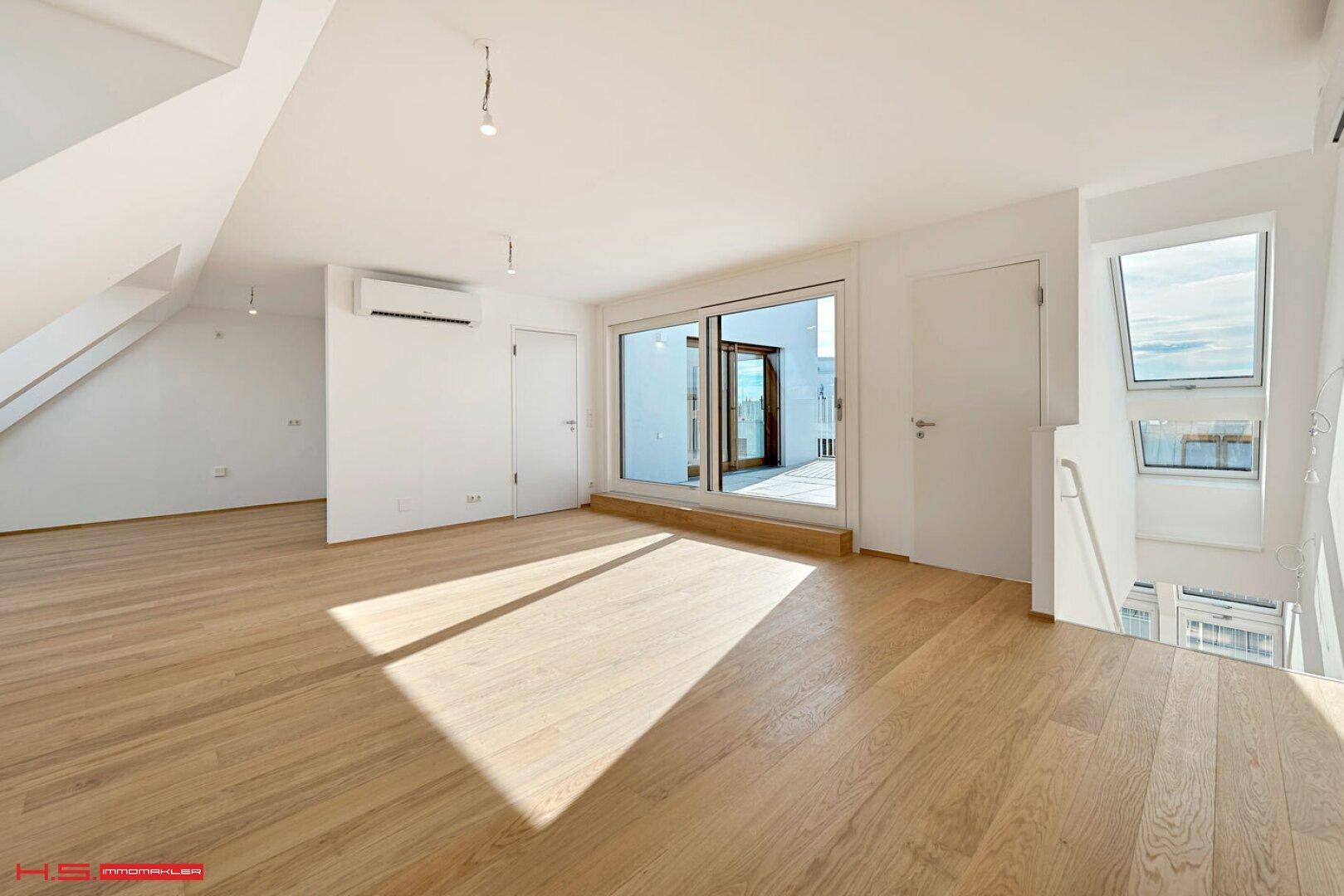 Offener Wohnbereich mit Holzparkett, Klimaanlage und Zugang zu einer sonnigen Terrasse.