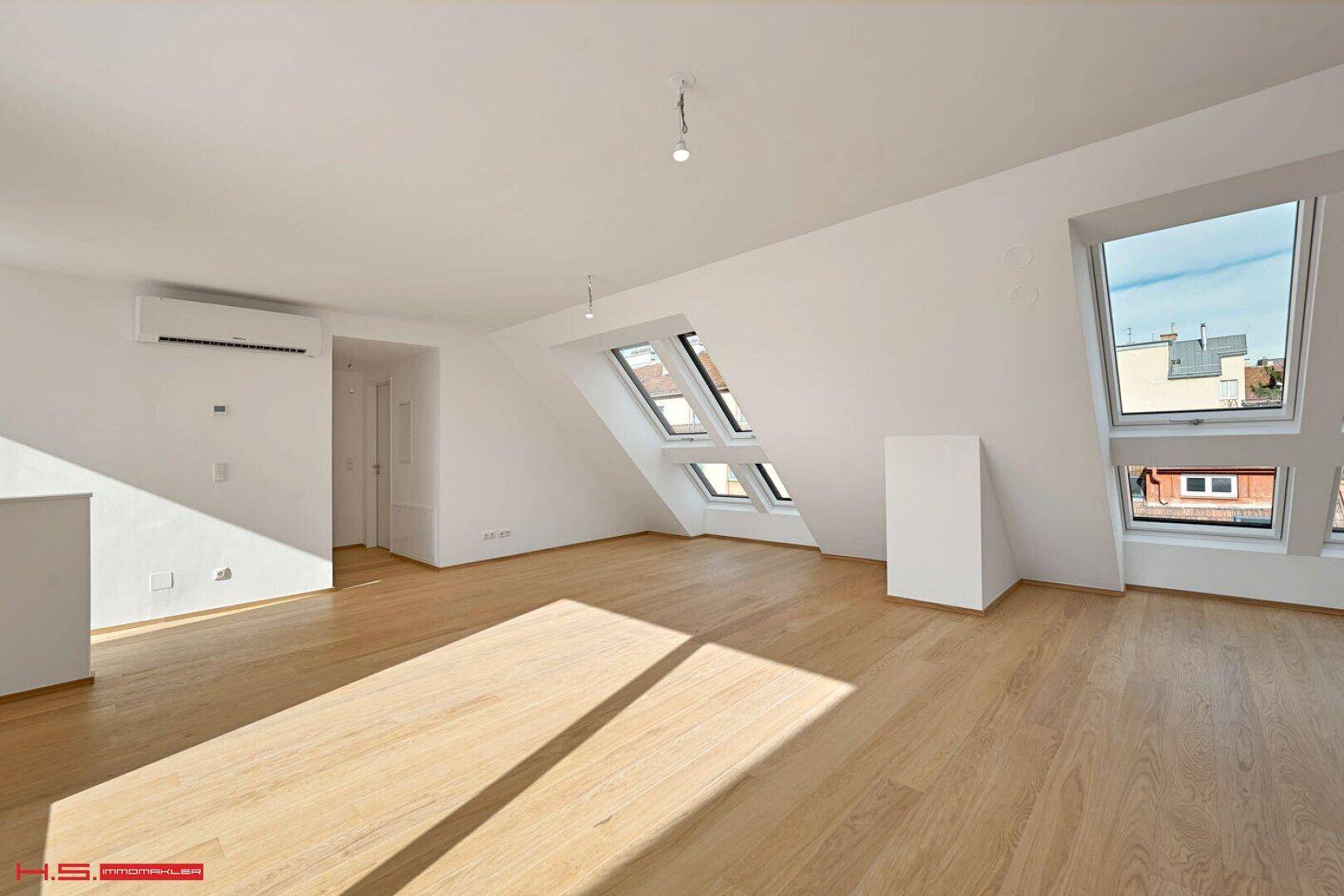 Lichtdurchfluteter Wohnbereich mit Dachschrägen, Holzparkett und Klimaanlage.