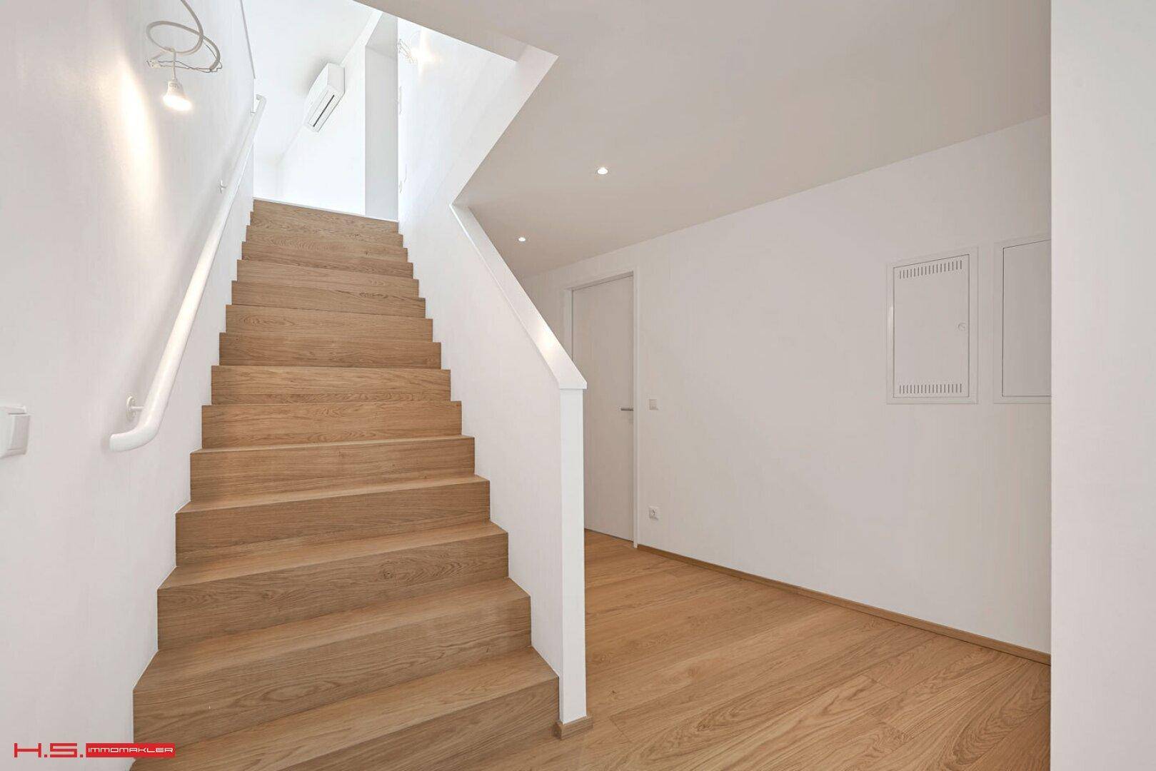 Moderne Holztreppe mit weißen Geländern und Wänden, die in die obere Etage führt.