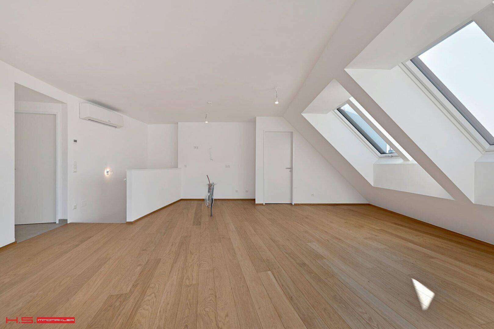 Geräumiger Wohnbereich mit Holzboden, Dachschrägen, Dachfenstern und Klimaanlage.