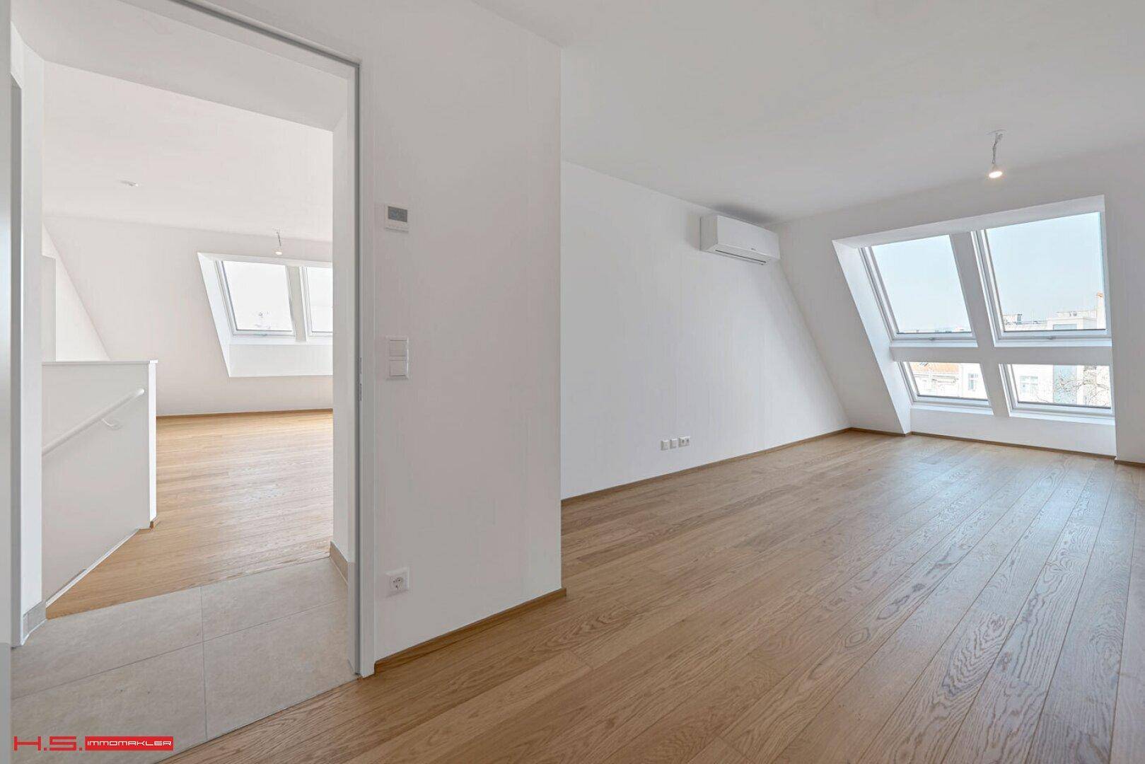 Heller Raum mit Holzboden, Dachschrägen, großen Dachfenstern und Klimaanlage.