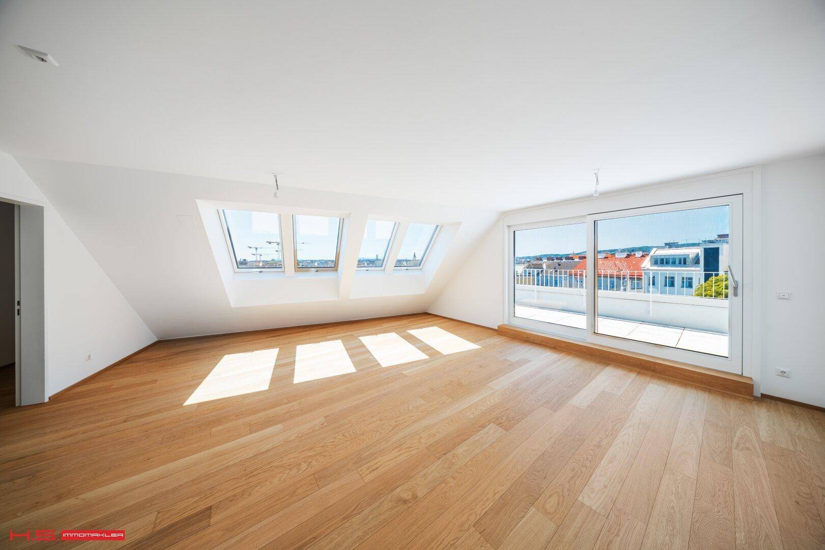 Heller Wohnraum mit Holzboden, Dachschrägen, großen Dachfenstern und Zugang zur Terrasse.