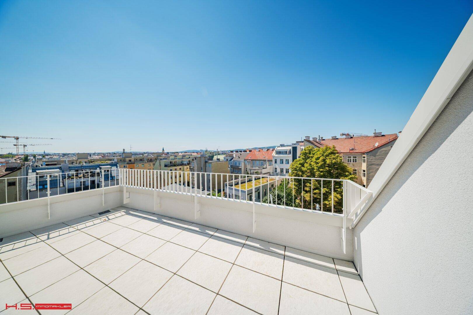 Sonniger Dachterrassenbereich mit weißen Fliesen und Geländer, bietet einen weiten Stadtblick.