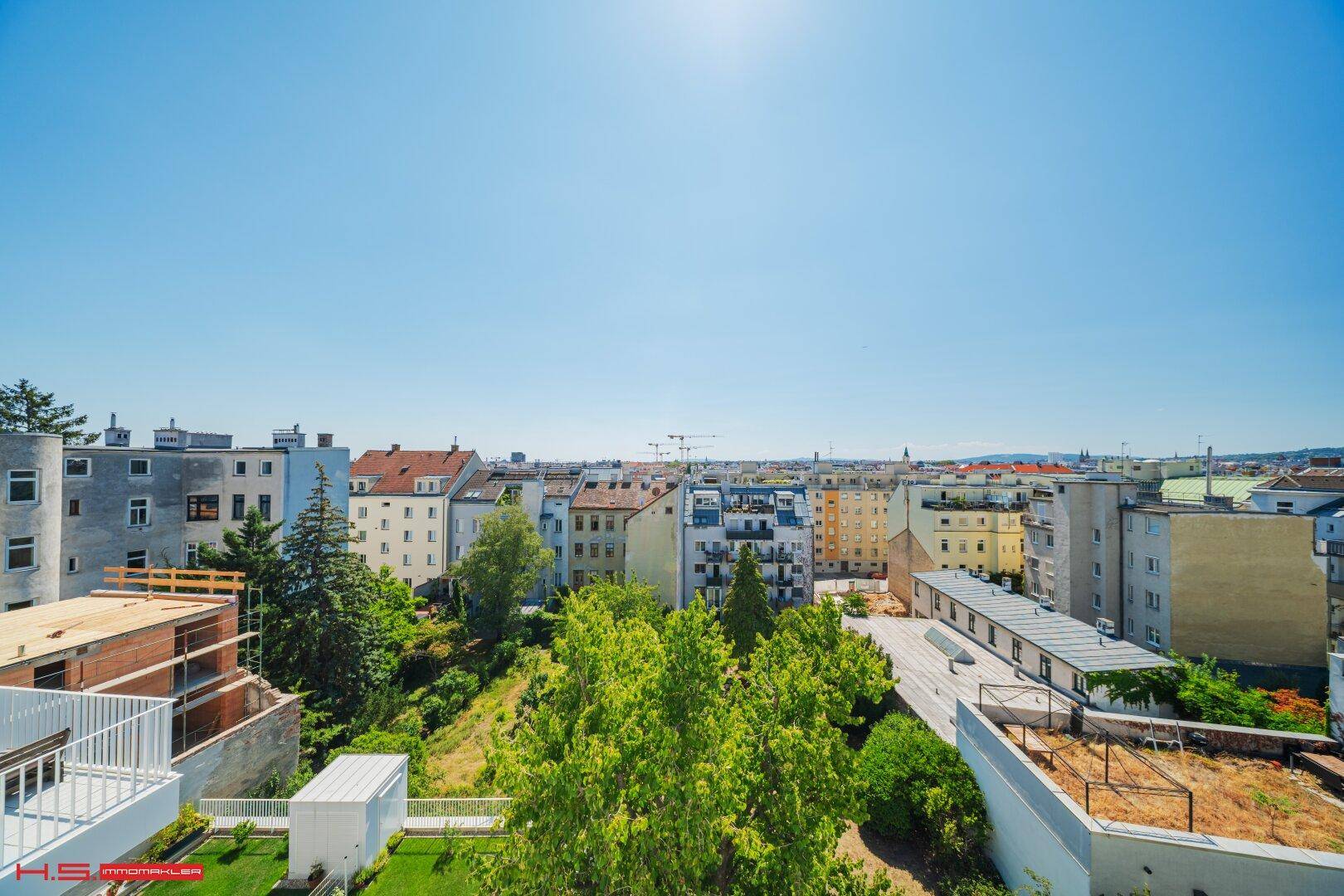 Panoramablick über die Stadt mit vielen Gebäuden und grünen Bäumen unter blauem Himmel.