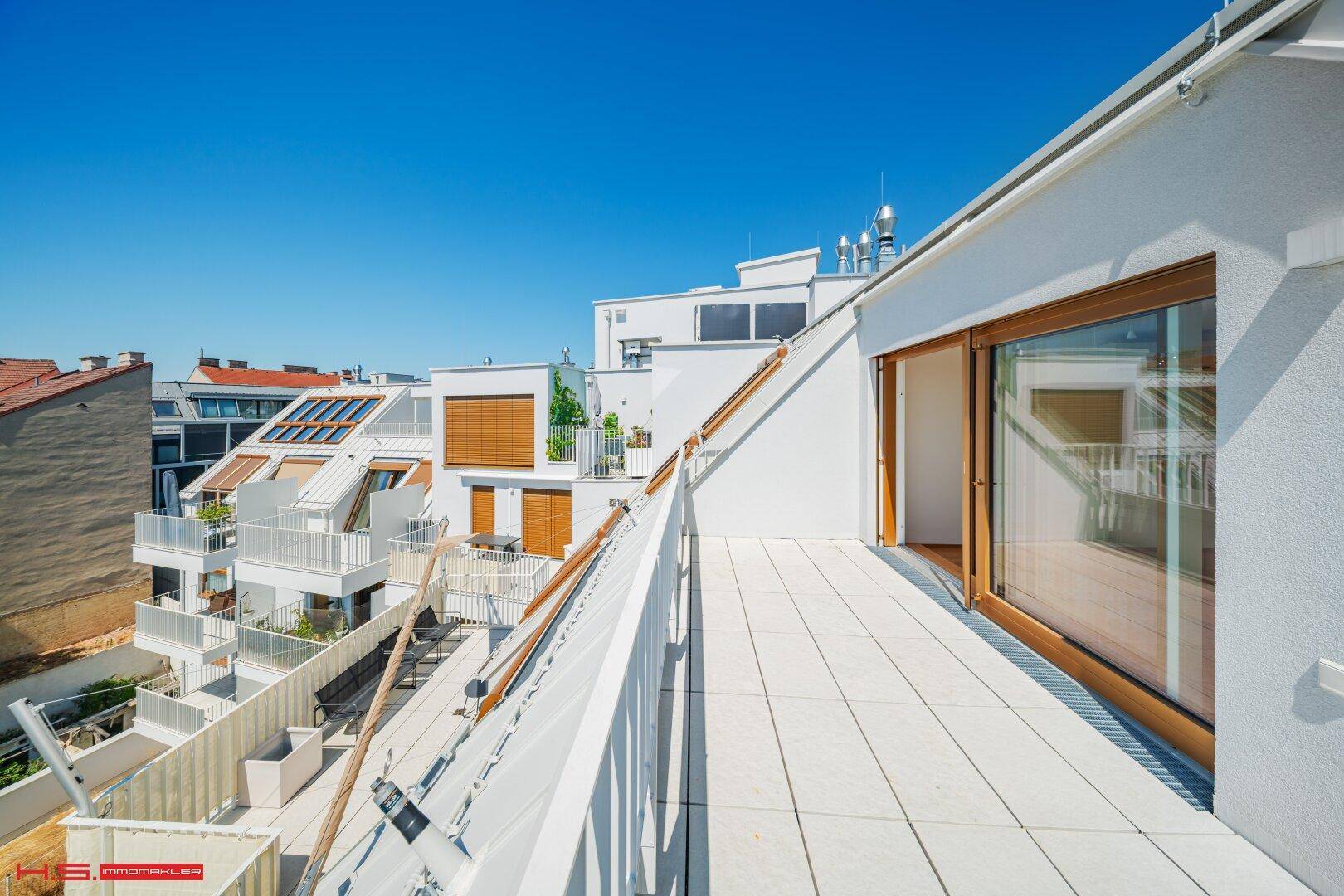 Mehrere Terrassen und Balkone mit weißen Geländern und Holzschiebetüren an einem modernen Gebäude.