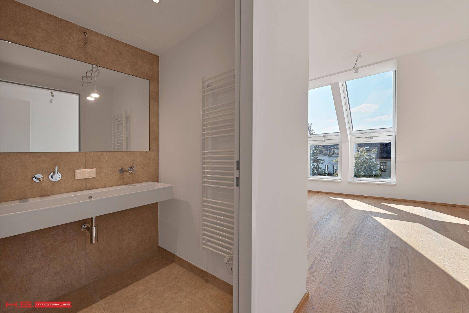 Modernes Badezimmer mit großem Spiegel, Waschbecken und Zugang zu einem hellen Raum.