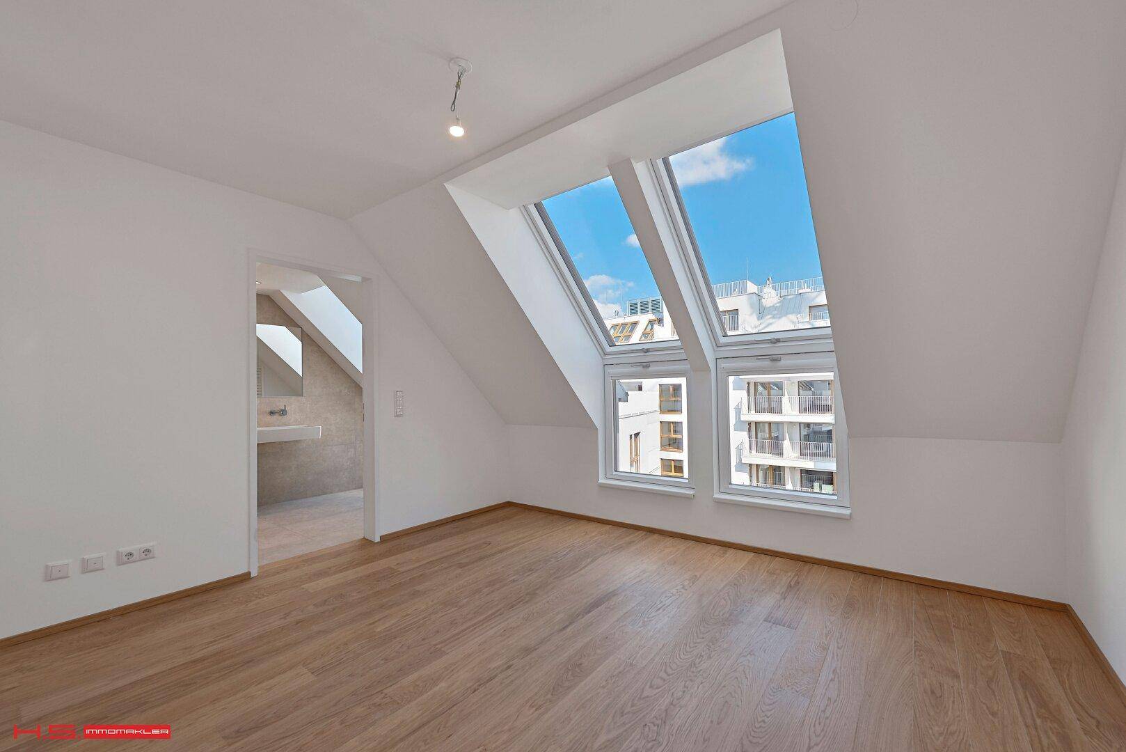 Helles Zimmer im Dachgeschoss mit Holzboden und großen Dachfenstern für viel Licht.