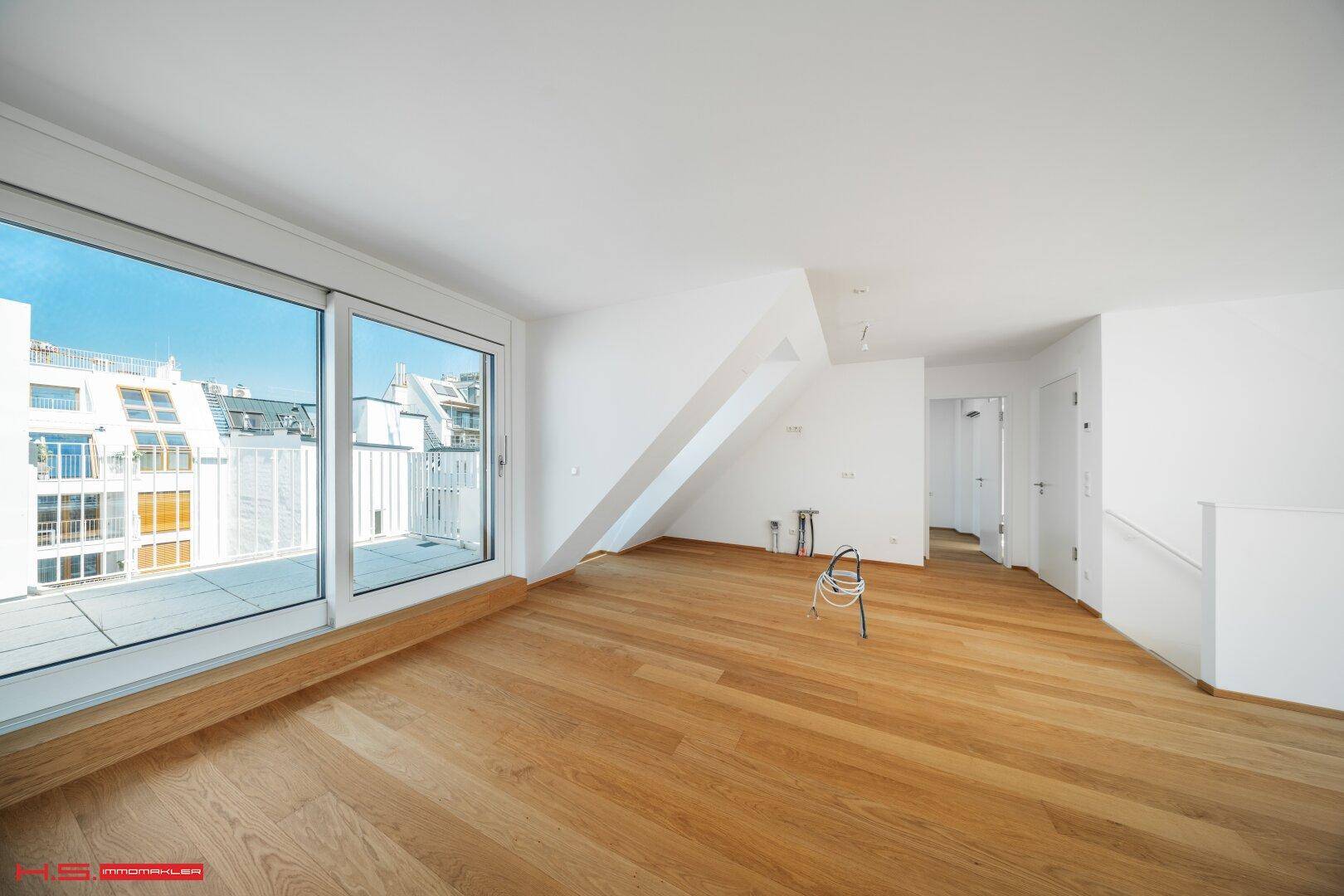 Geräumiger Wohnbereich mit Holzboden, Dachschräge und Zugang zu einer großen Terrasse.