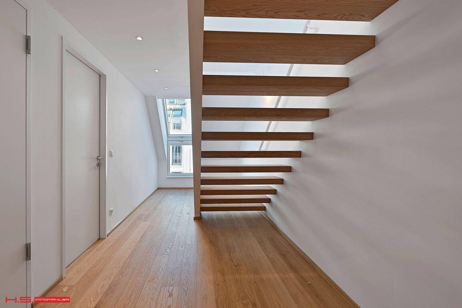 Heller Flur mit Holztreppe und Holzboden, der zu den oberen Etagen führt.