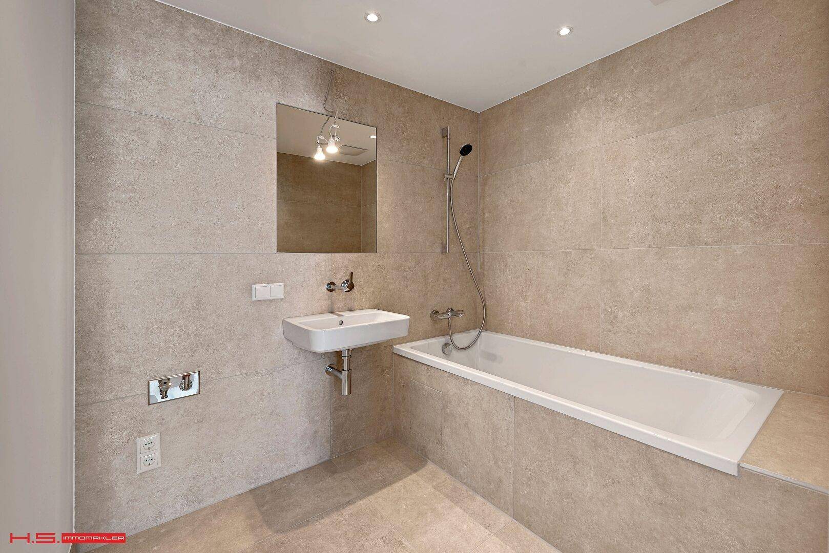 Modernes Badezimmer mit Badewanne, Wandwaschbecken und großen grauen Fliesen.