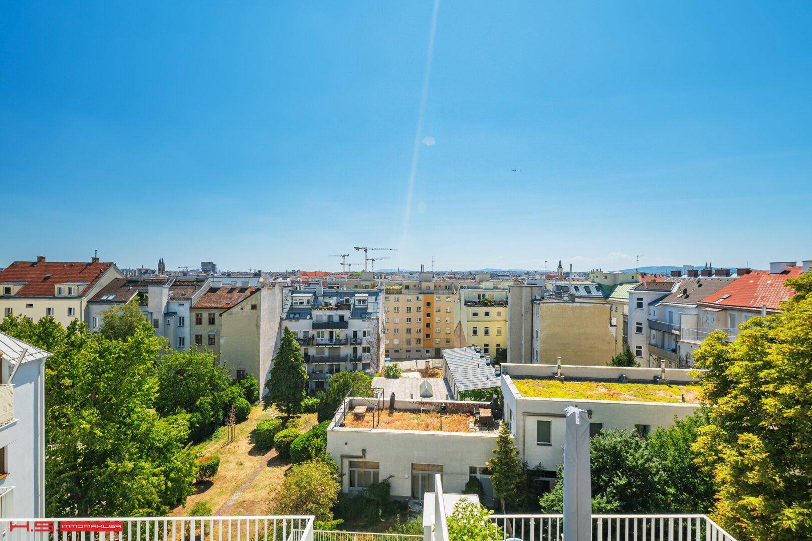 Weiter Blick über die Stadt und grüne Gärten von einer sonnigen Dachterrasse.