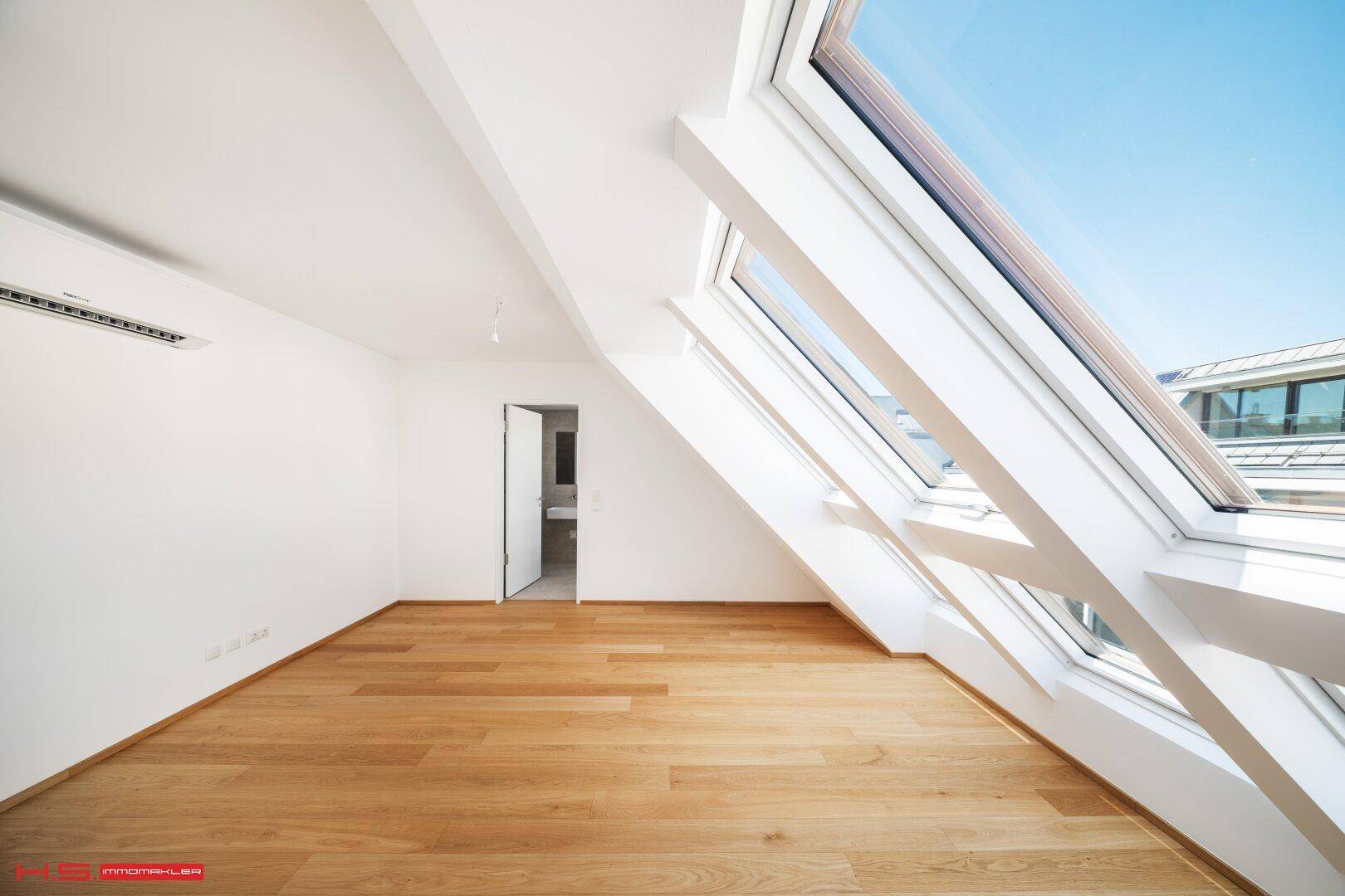 Helles Schlafzimmer mit Holzboden, schrägen Wänden und großen Dachfenstern.
