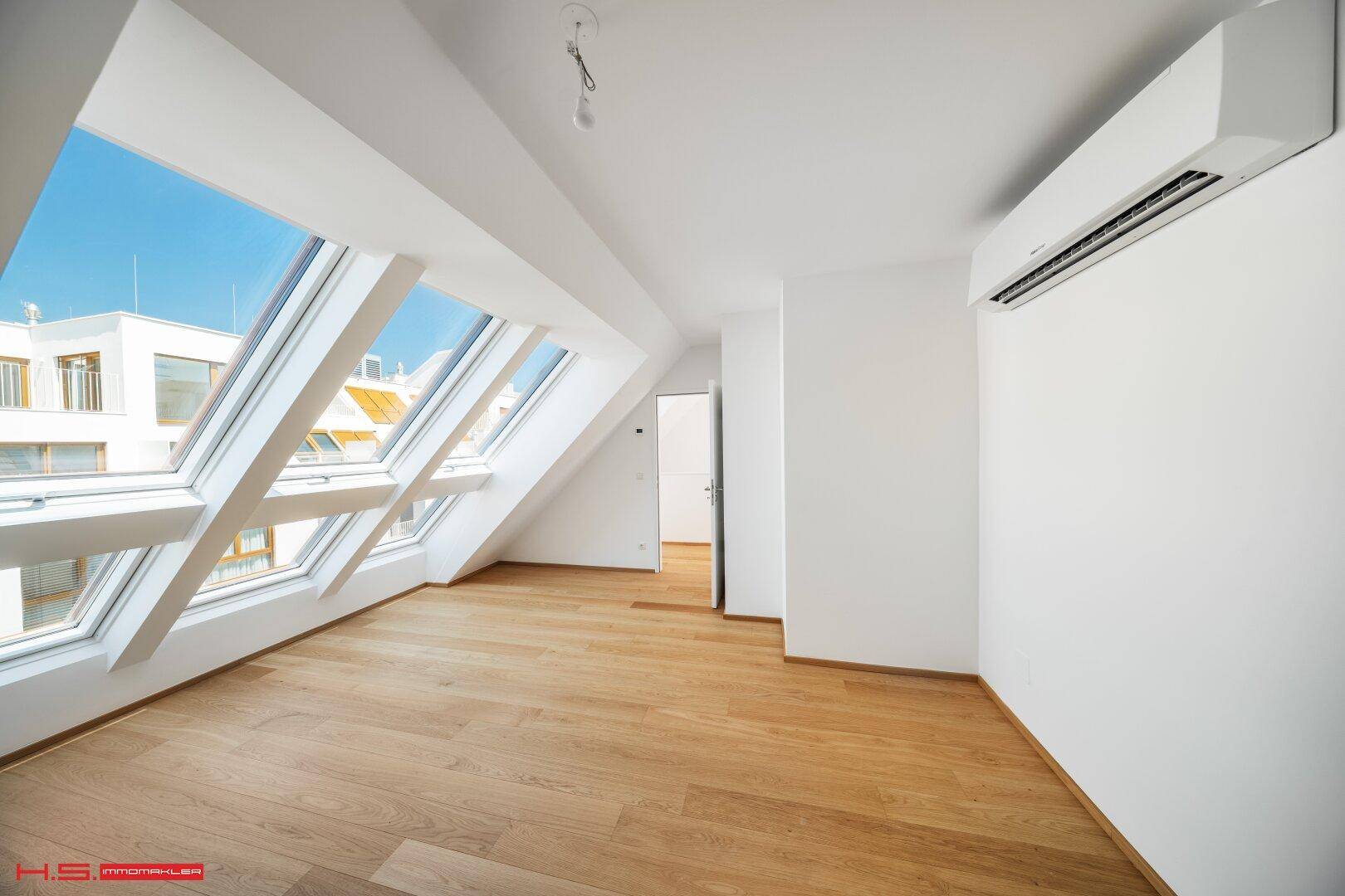 Geräumiges Schlafzimmer mit Holzboden, Klimaanlage und viel Tageslicht durch Dachfenster.