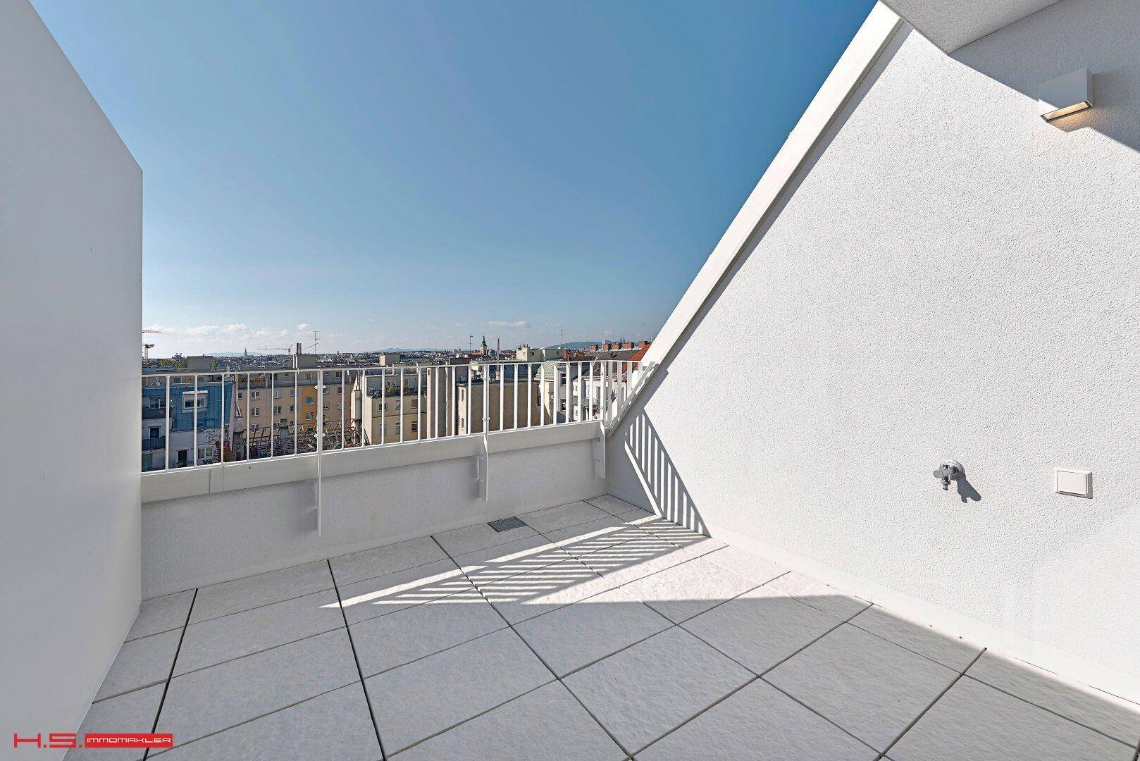 Sonniger Terrassenbereich mit hellen Fliesen und Blick auf die umliegenden Gebäude.
