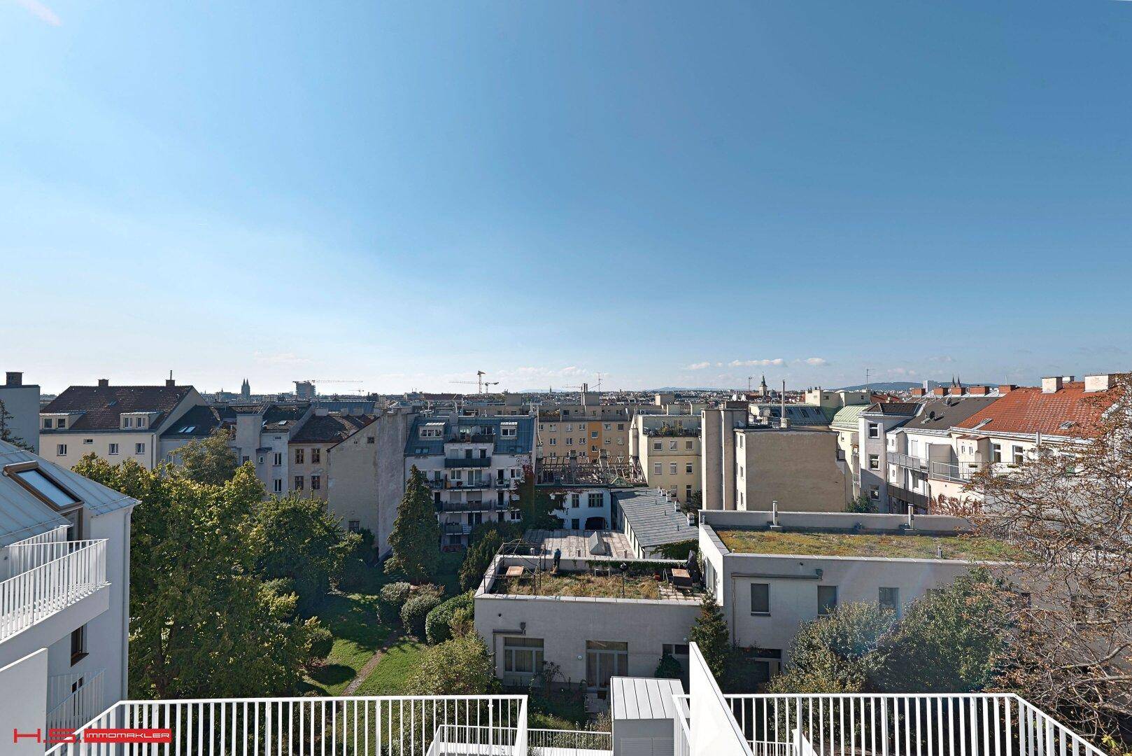 Panoramablick über die Stadt und grüne Innenhöfe von einer sonnigen Dachterrasse.