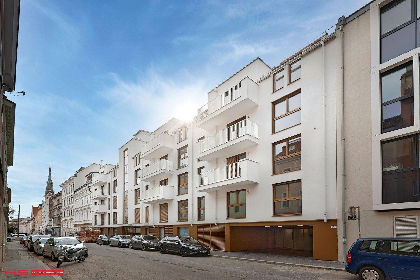 Moderne Wohnanlage mit weißer Fassade, Balkonen und Tiefgaragenzufahrt an einer Stadtstraße.