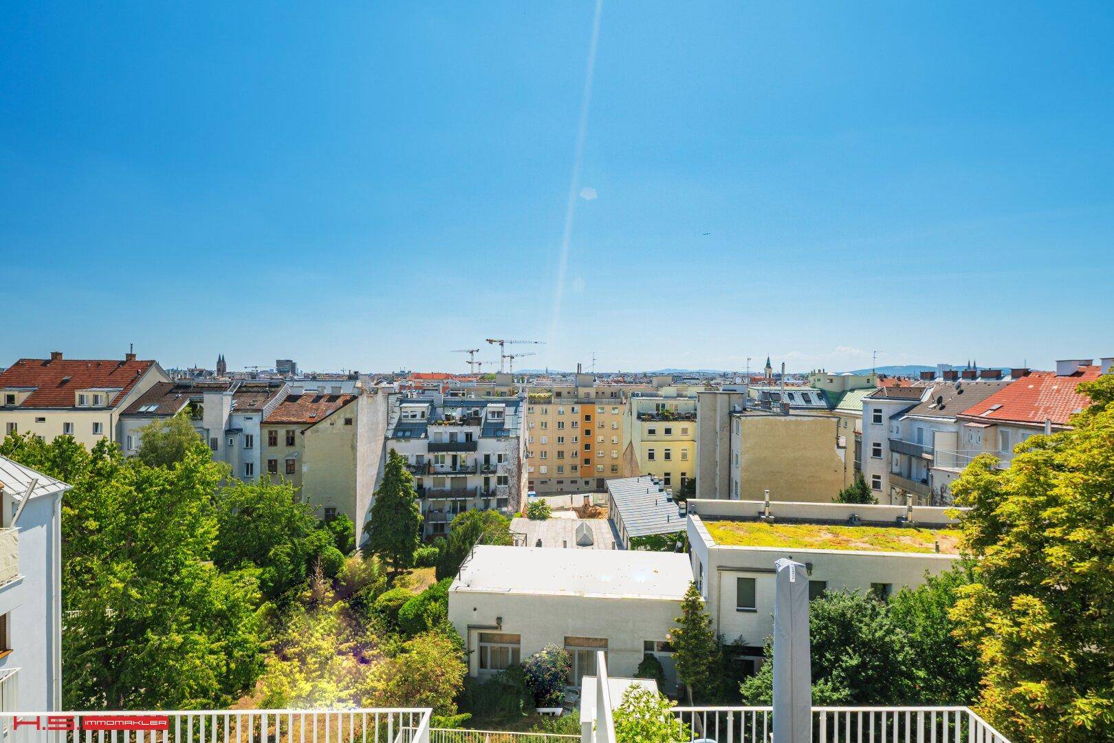 Panoramablick über die Stadt mit grünen Bäumen und umliegenden Gebäuden an einem sonnigen Tag.