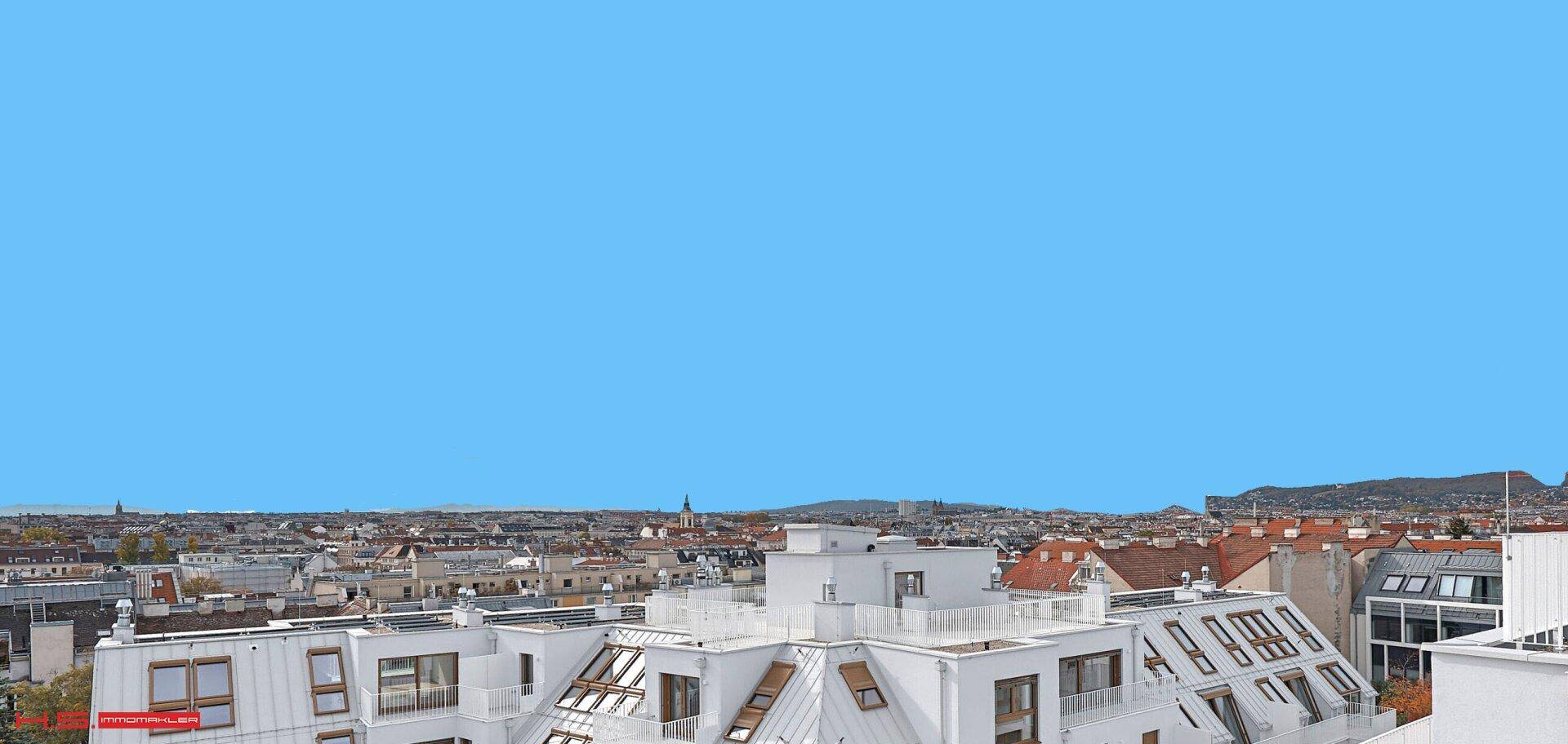 Blick über die Dächer der Stadt mit modernen Gebäuden und weitem Horizont unter blauem Himmel.