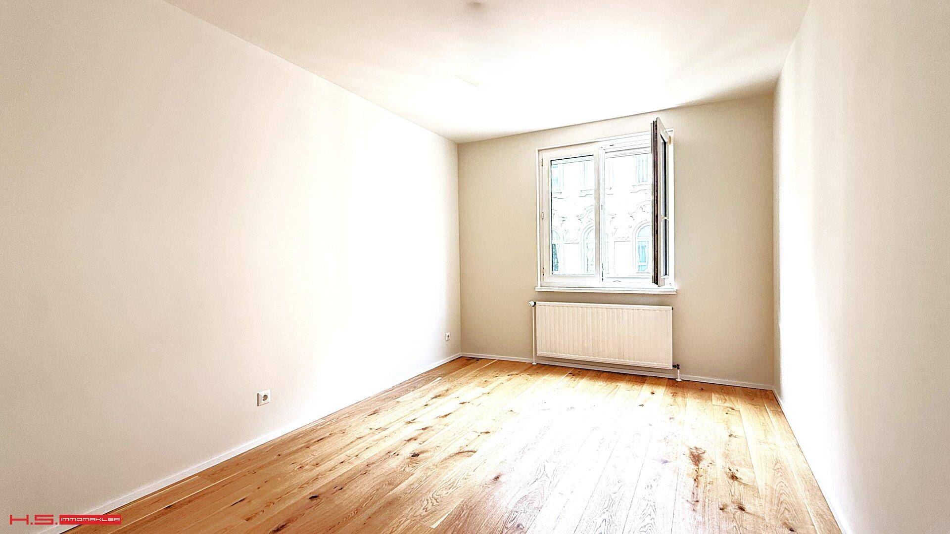 Freundliches Zimmer mit Holzboden und großem Fenster, das viel Tageslicht hereinlässt.