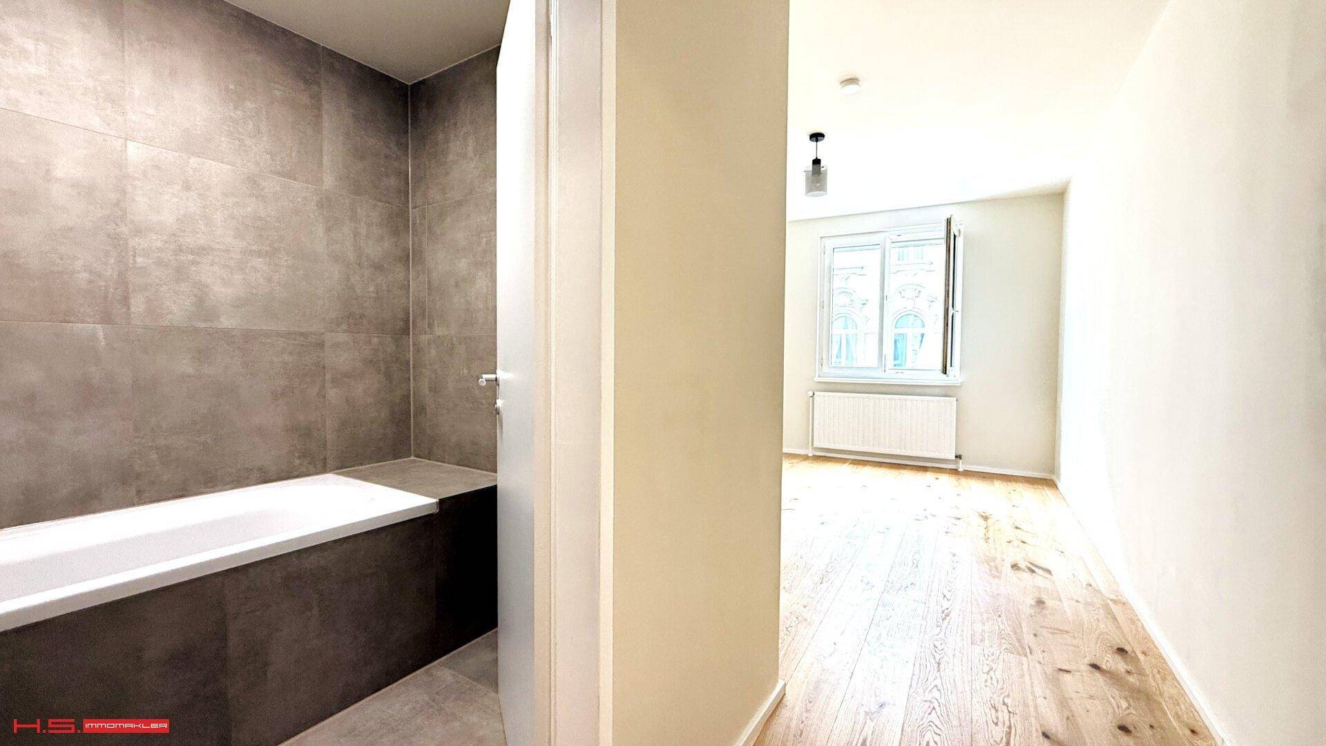 Heller Flur mit Holzboden, der zu einem Zimmer mit Fenster und zum modernen Badezimmer führt.