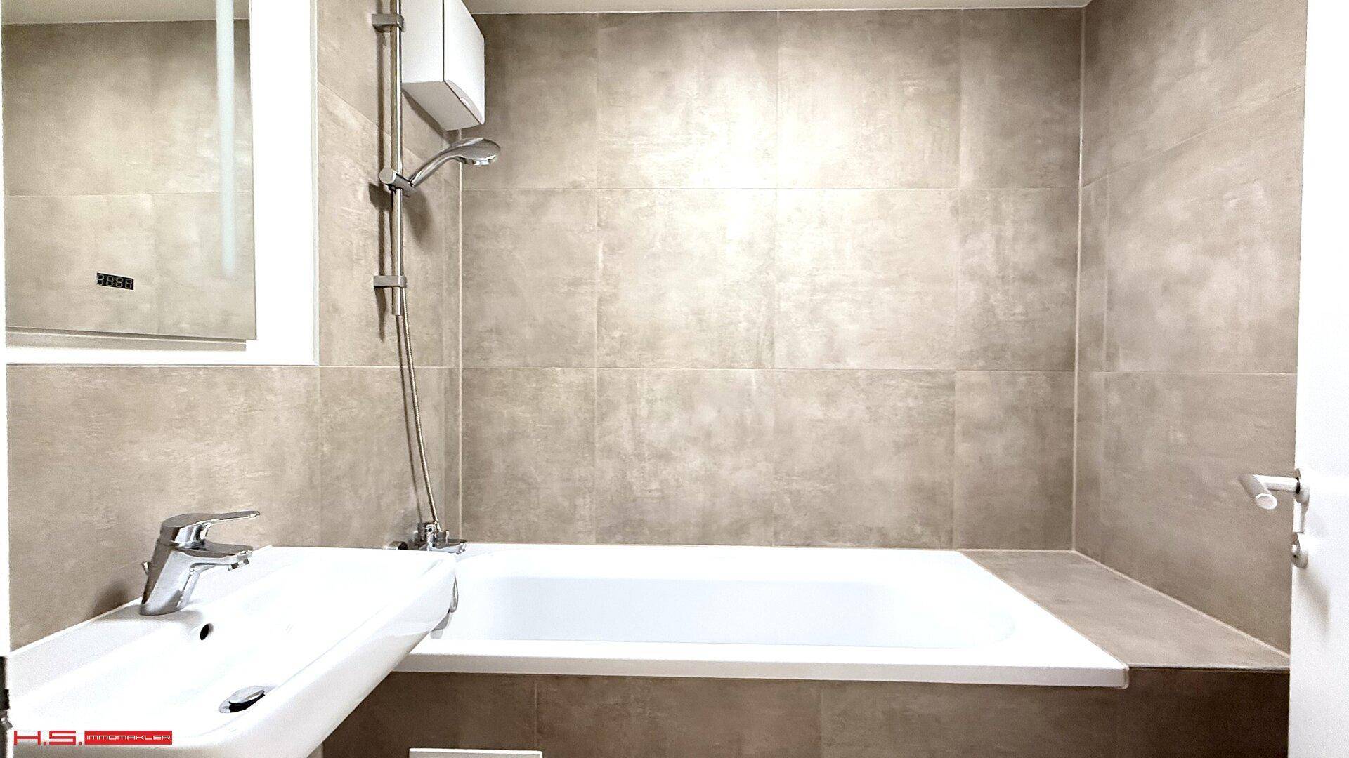 Modernes Badezimmer mit Badewanne, eleganten grauen Fliesen und integriertem Waschbecken.