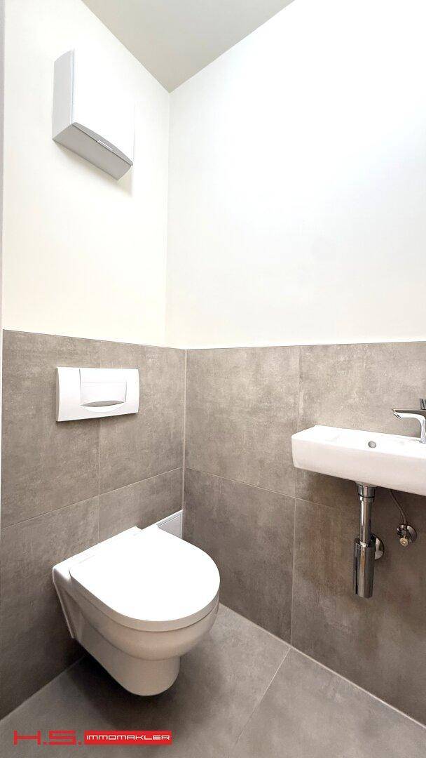 Modernes Gäste-WC mit wandhängender Toilette, kleinem Waschbecken und grauen Fliesen.
