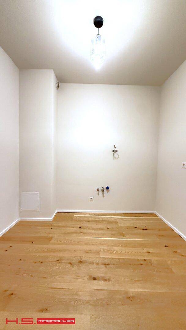 Leerer Raum mit Holzboden und Anschlüssen für eine Küche, bereit für die Installation.