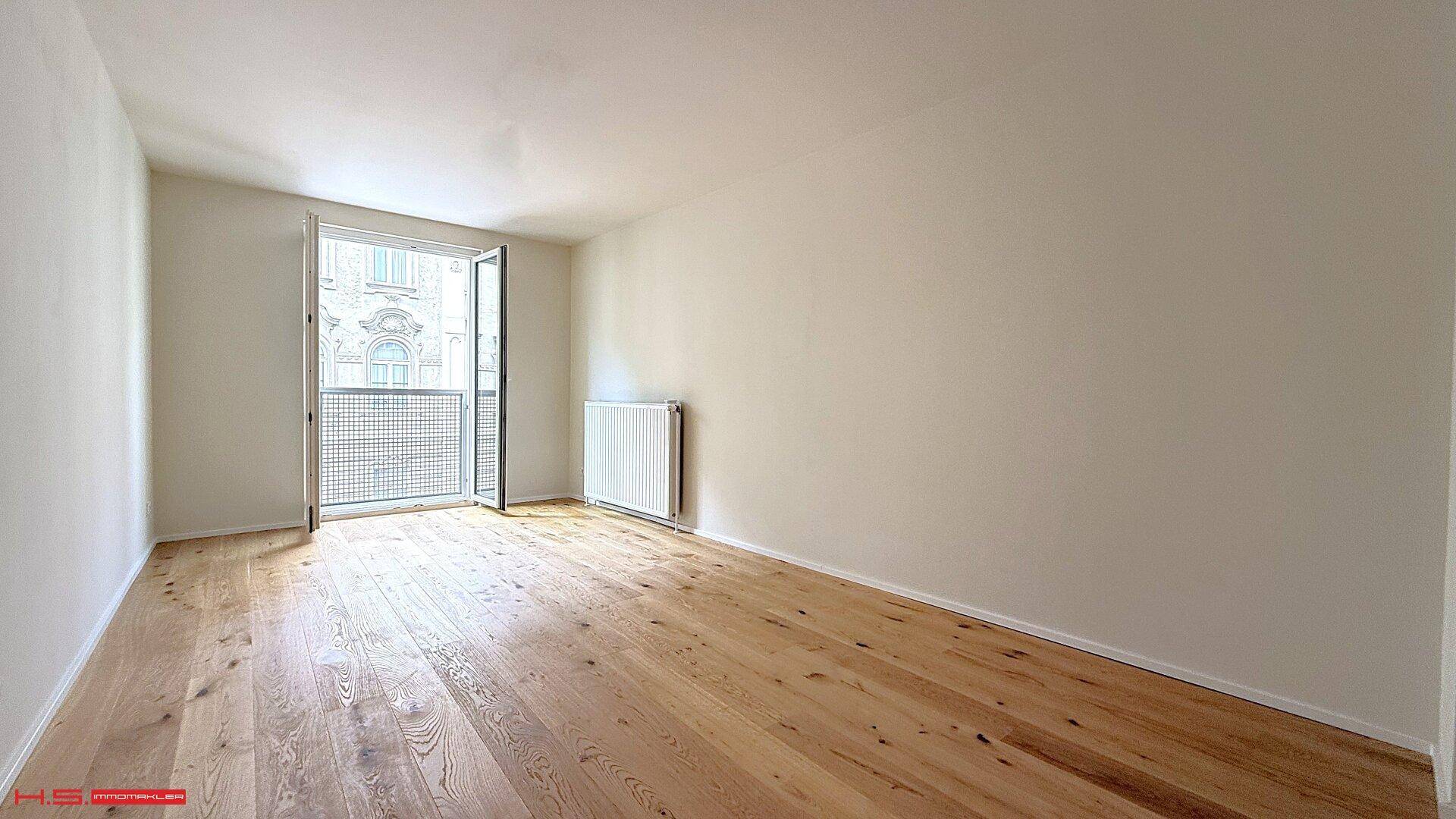 Geräumiges Zimmer mit hellem Holzboden, Heizkörper und Zugang zu einem französischen Balkon.