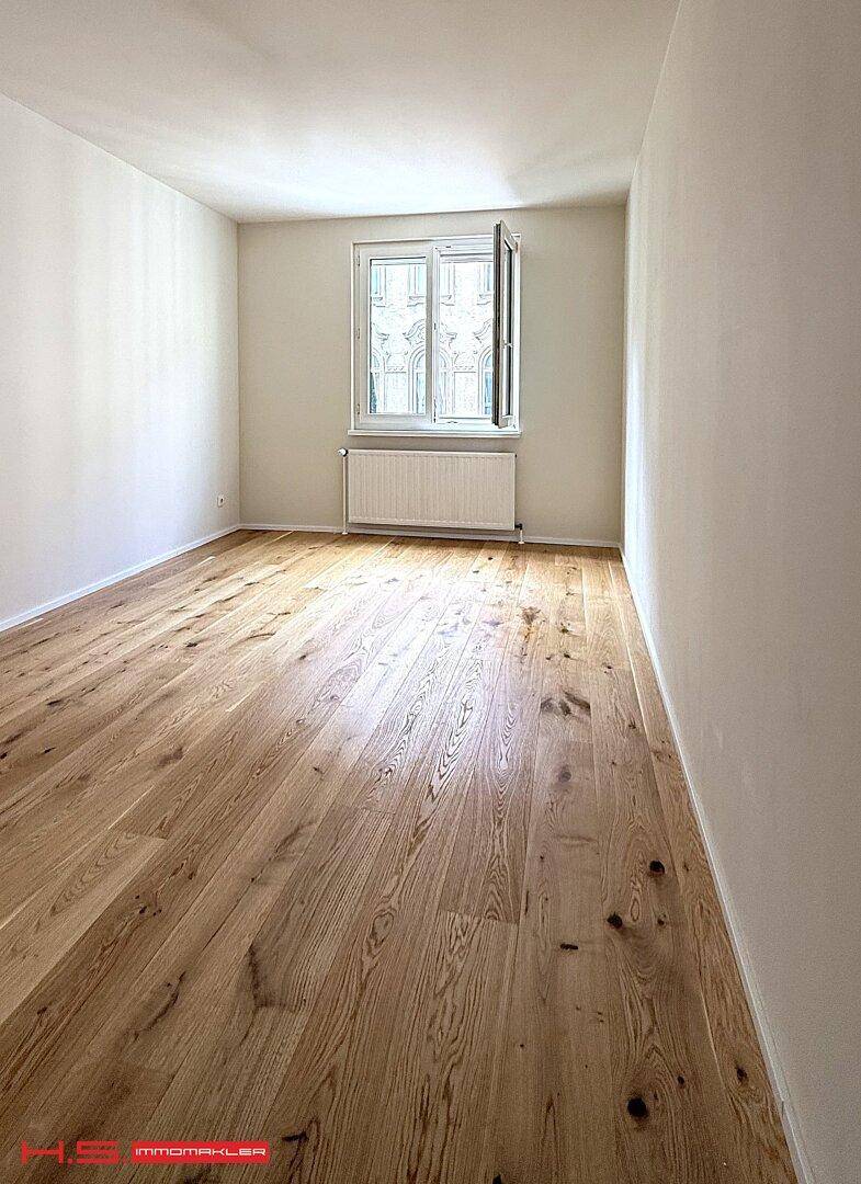 Lichtdurchflutetes Zimmer mit Holzboden und Fenster, das einen Blick auf die Stadt bietet.