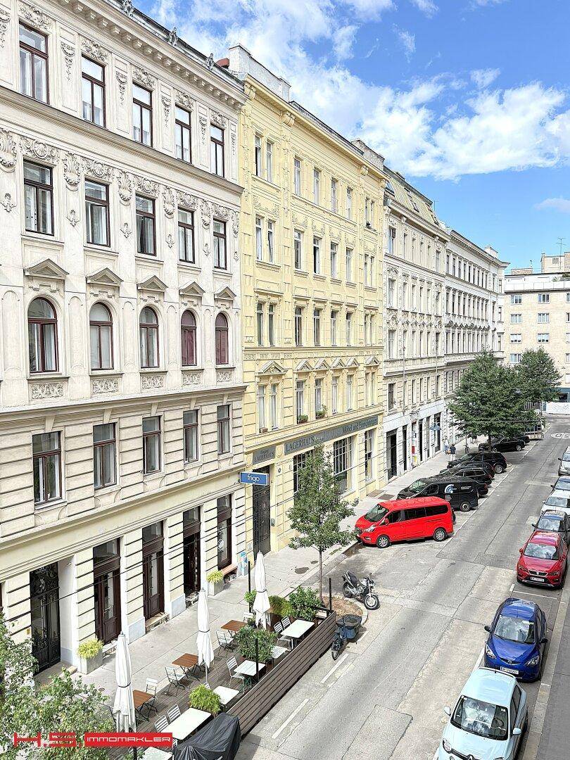 Historische Straßenansicht mit eleganten Gebäudefassaden und geparkten Autos entlang der Straße.