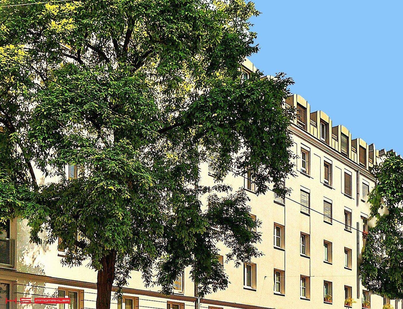 Fassade eines Mehrfamilienhauses mit grünen Bäumen davor und klassischer Architektur.