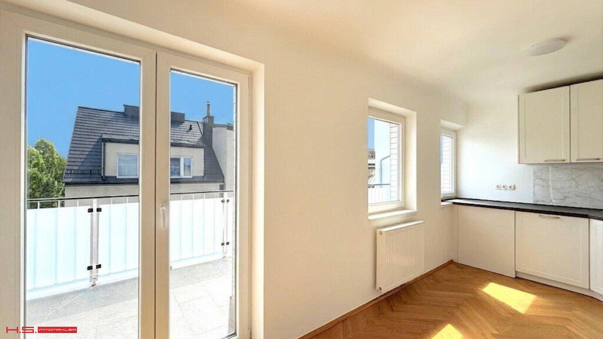 Helle Küche mit modernen weißen Schränken, Fischgrätparkett und Zugang zu einem Balkon.