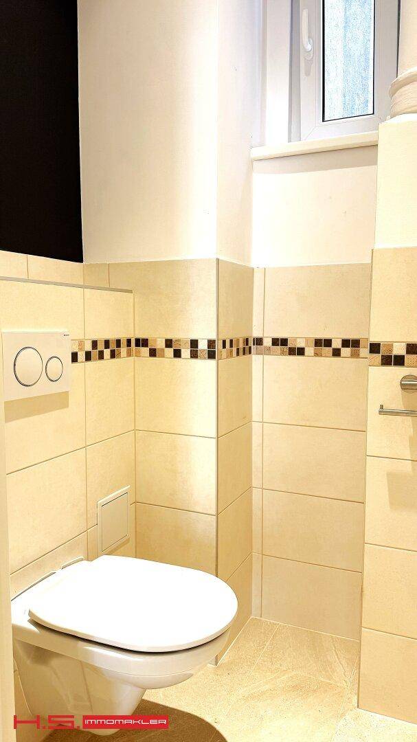 Modernes Gäste-WC mit Wand-WC, beigen Fliesen und einem kleinen Fenster.