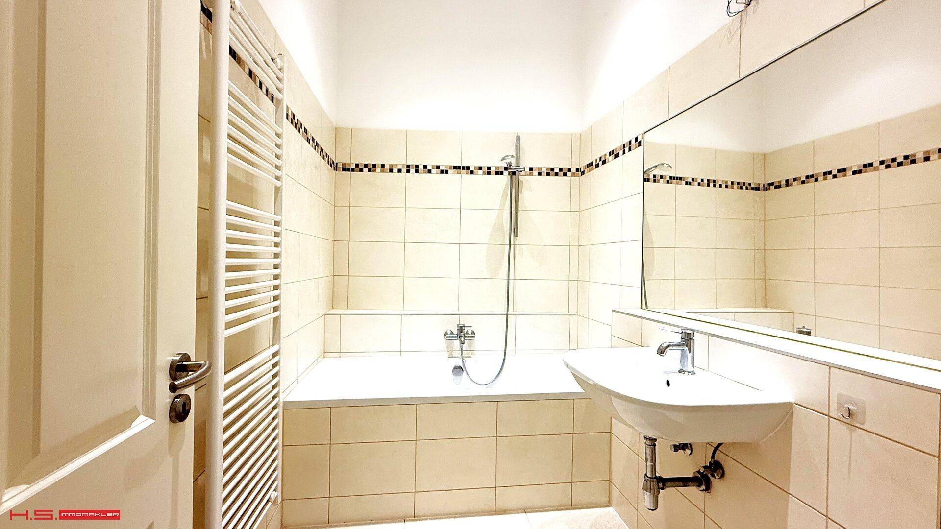 Helles Badezimmer mit Badewanne, Waschbecken, großem Spiegel und Handtuchheizkörper.