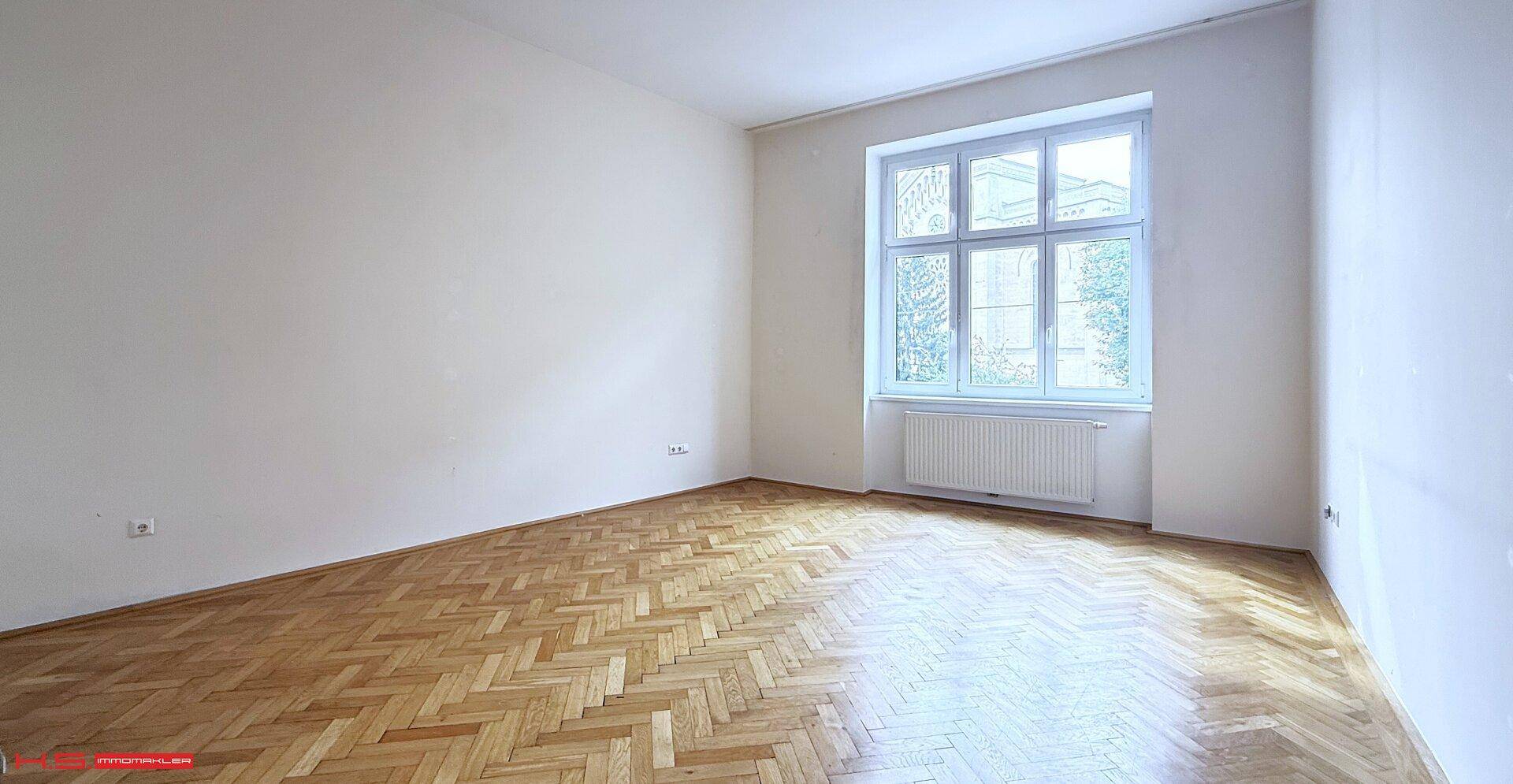 Geräumiges Zimmer mit hellem Fischgrätparkett und einem großen Fenster für viel Licht.