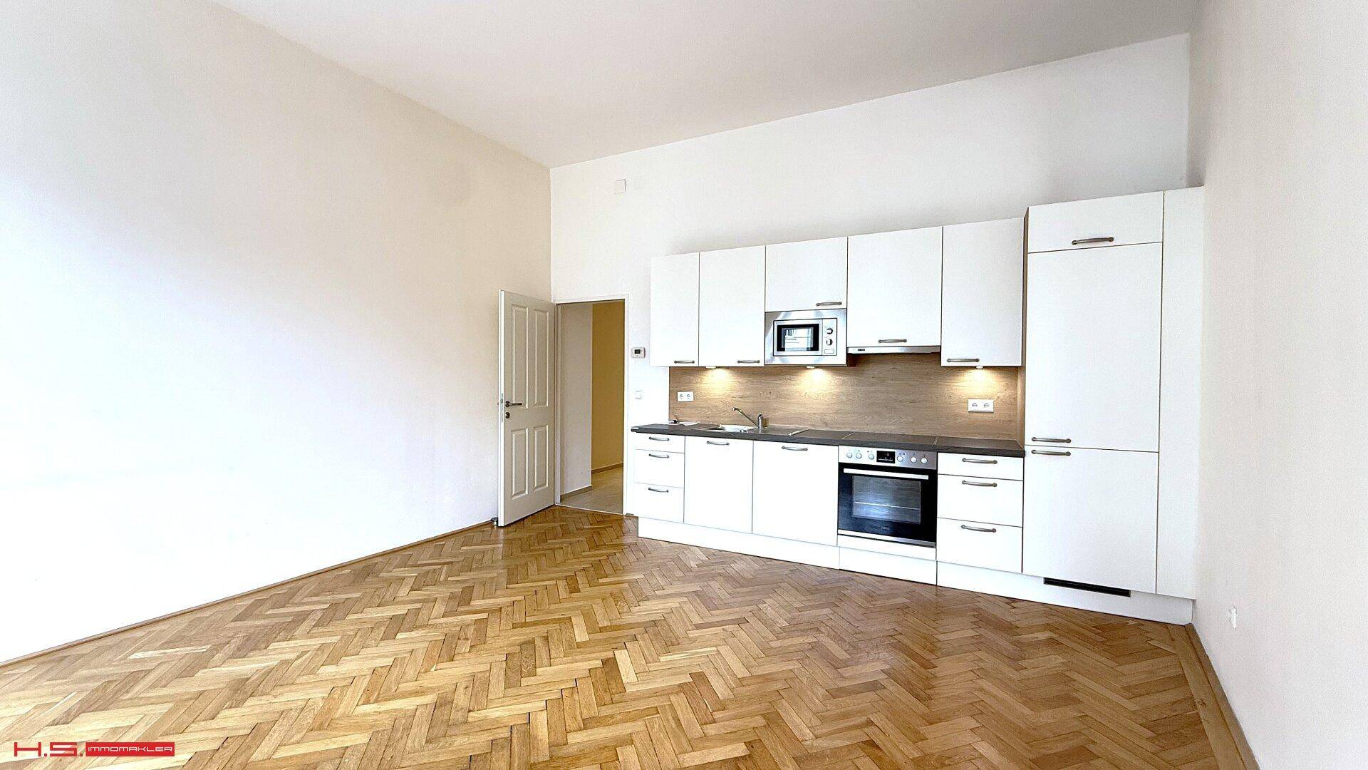 Moderne Küchenzeile mit weißen Schränken, integrierten Geräten und Fischgrätparkett.