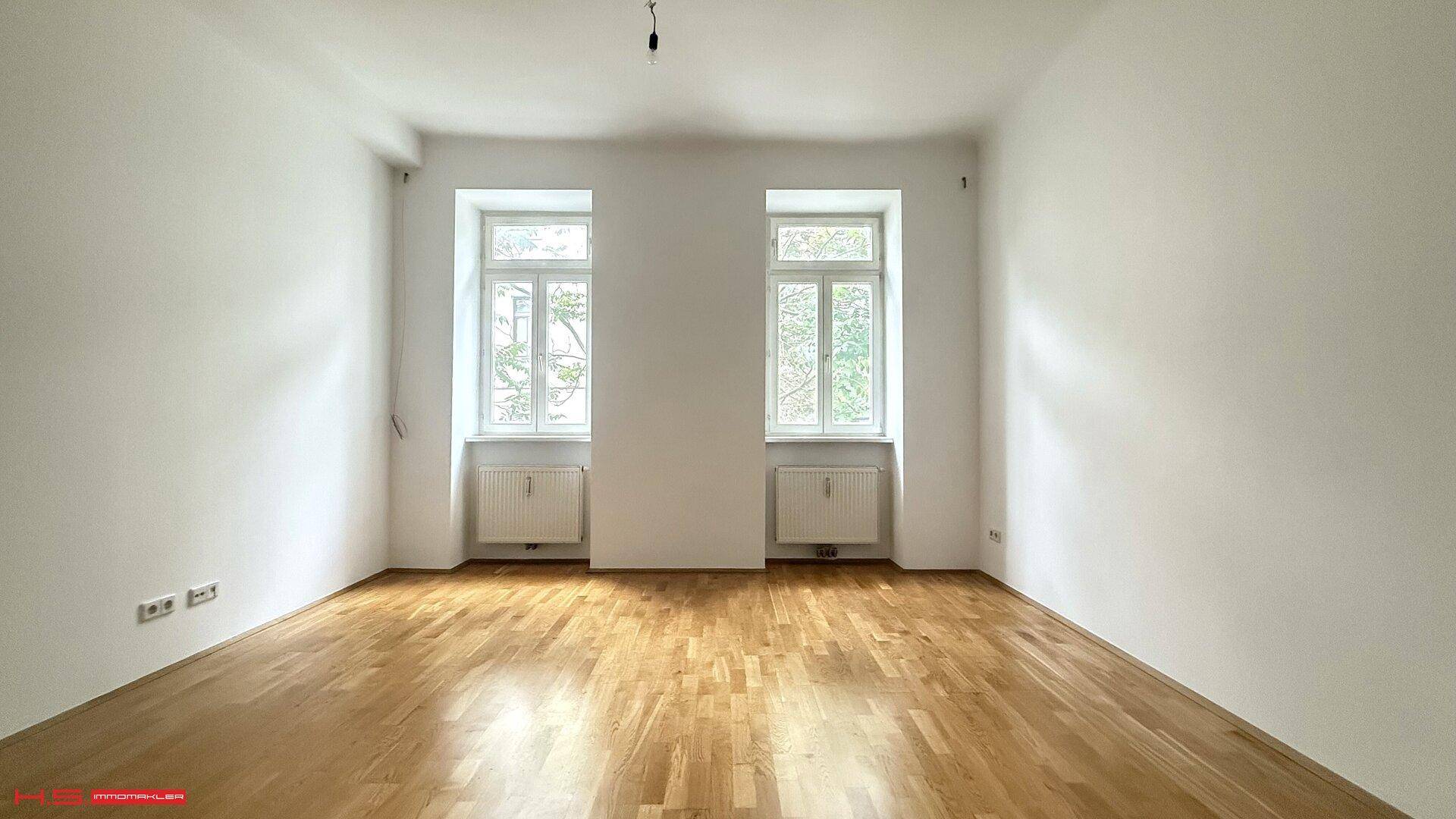 Geräumiger, heller Raum mit Holzboden und großen Fenstern, bereit zur individuellen Gestaltung.