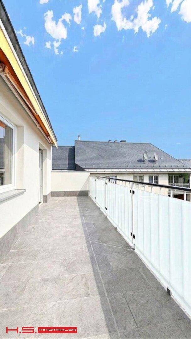Helle Terrasse mit grauen Fliesen und einer modernen weißen Brüstung unter klarem Himmel.