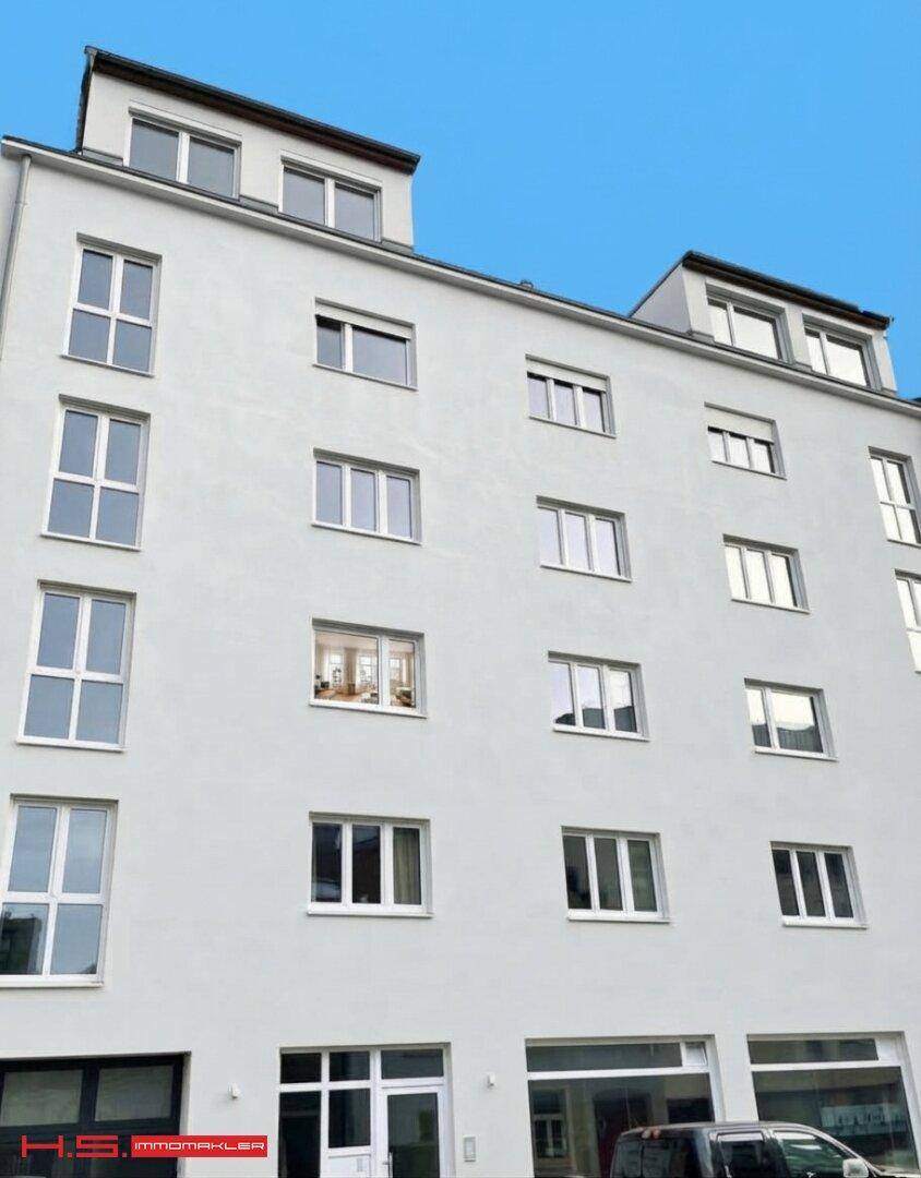 Moderne helle Fassade eines Mehrfamilienhauses mit vielen Fenstern und Dachgauben.