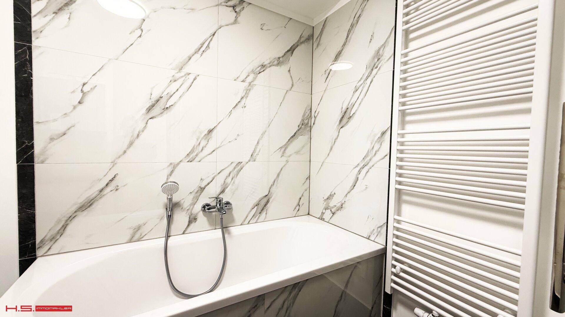 Moderne Badewanne mit Marmorfliesen und beheiztem Handtuchhalter in einem hellen Badezimmer.