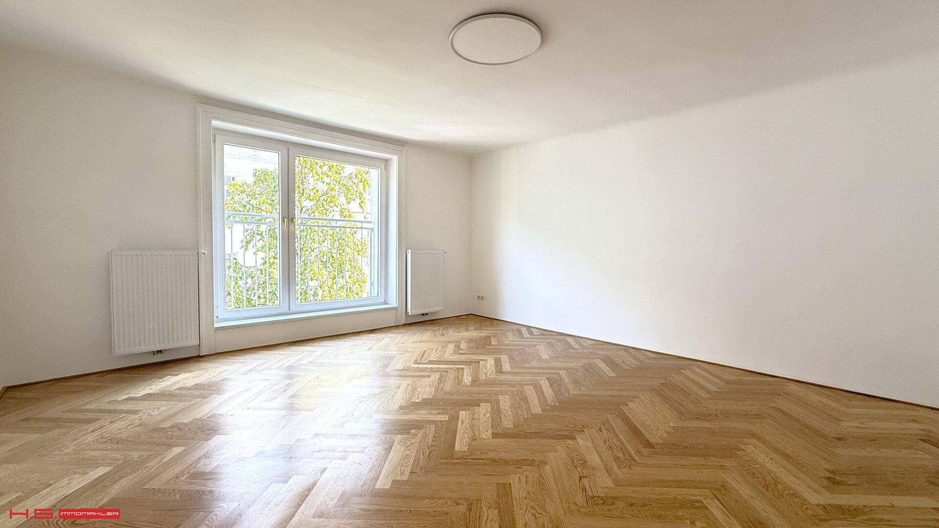 Helles Schlafzimmer mit Fischgrätparkett und großem Fenster, das viel Tageslicht hereinlässt.