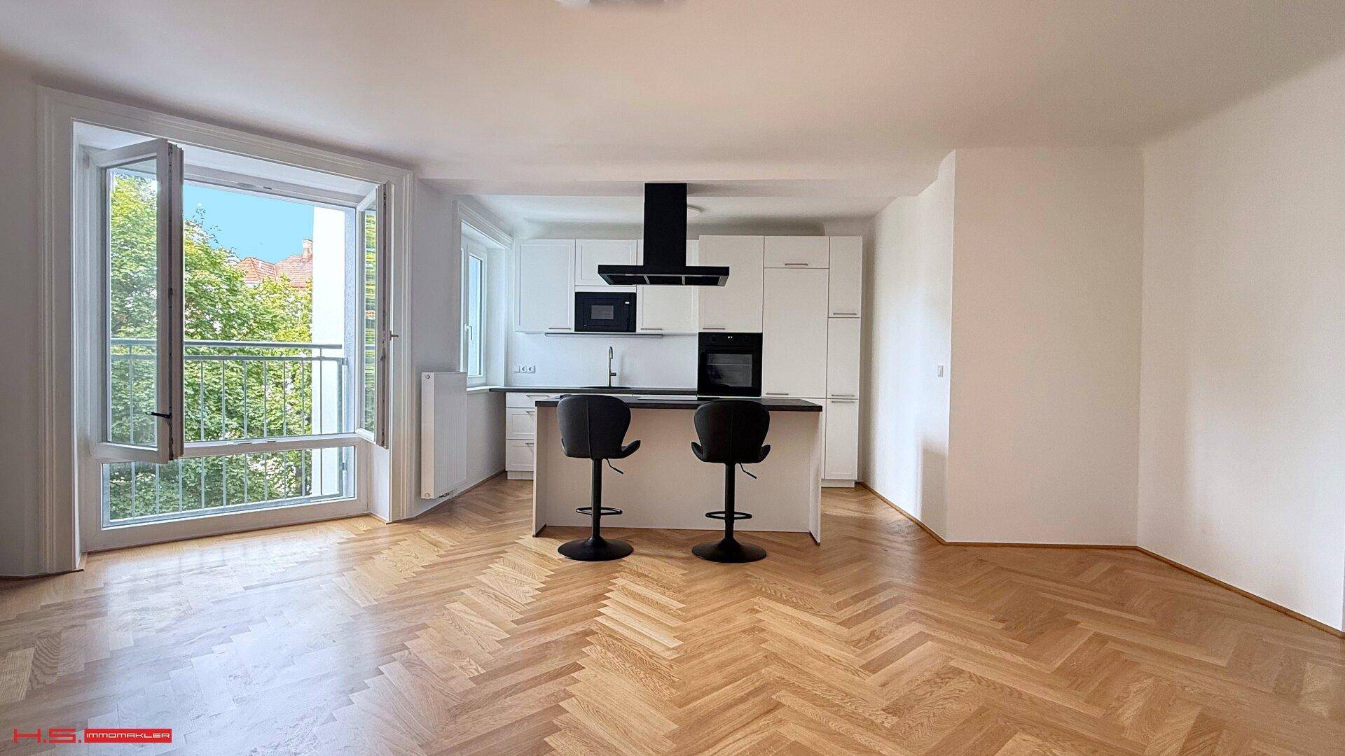 Offener Wohnbereich mit moderner Einbauküche, Kücheninsel und Blick ins Grüne durch die Fenster.