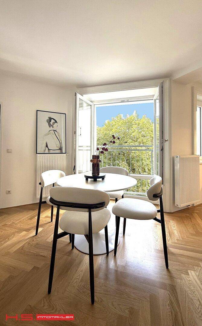 Gemütlicher Essbereich mit rundem Tisch und Stühlen, direkt am offenen Balkonfenster.
